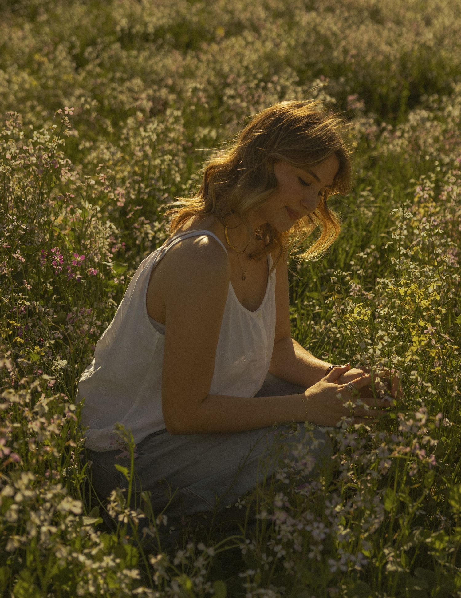 Person in white dress lying in a wildflower meadow during golden hour.
