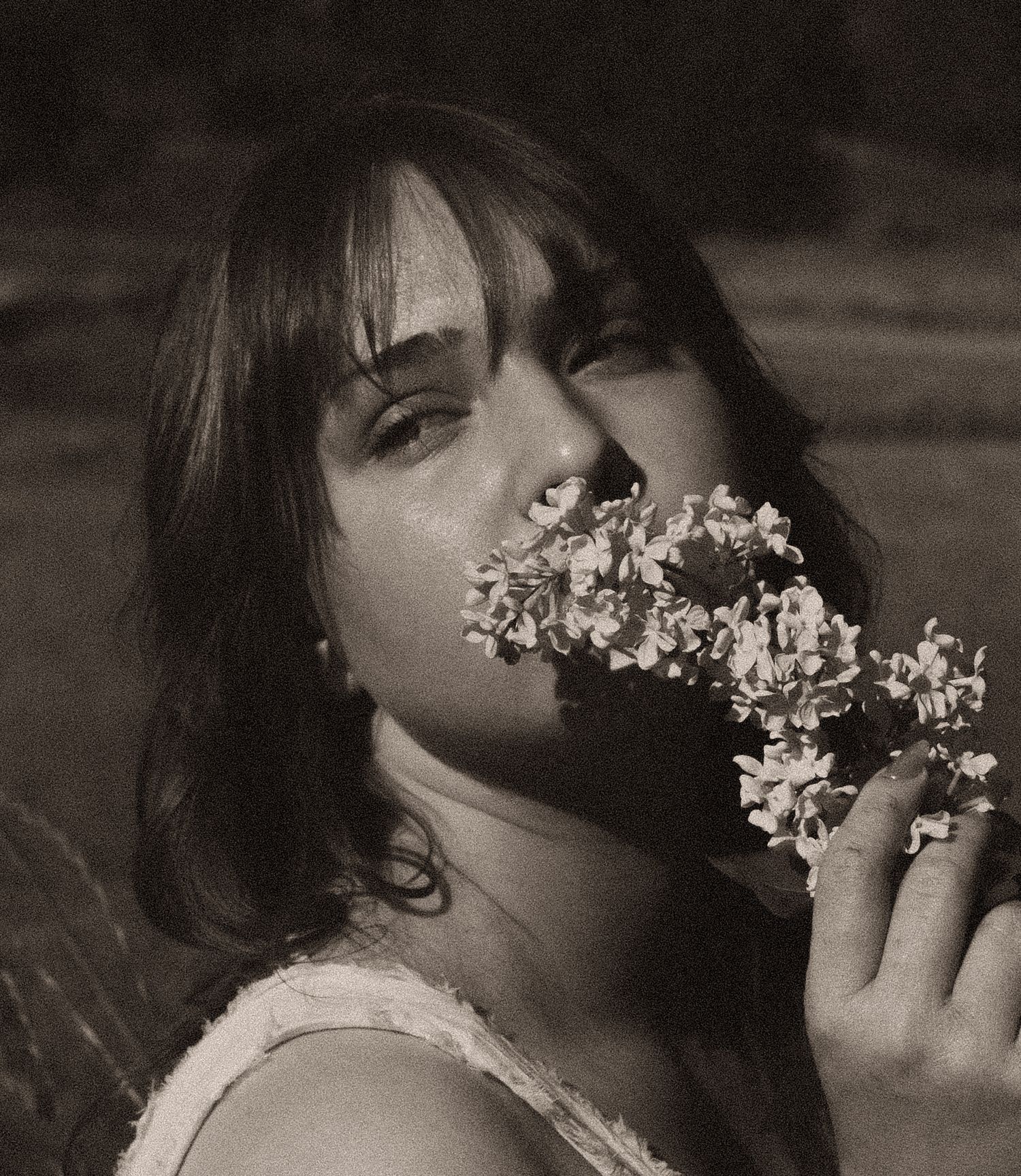 Young woman with bangs holding white flowers to her face in a dreamy black and white portrait photo.