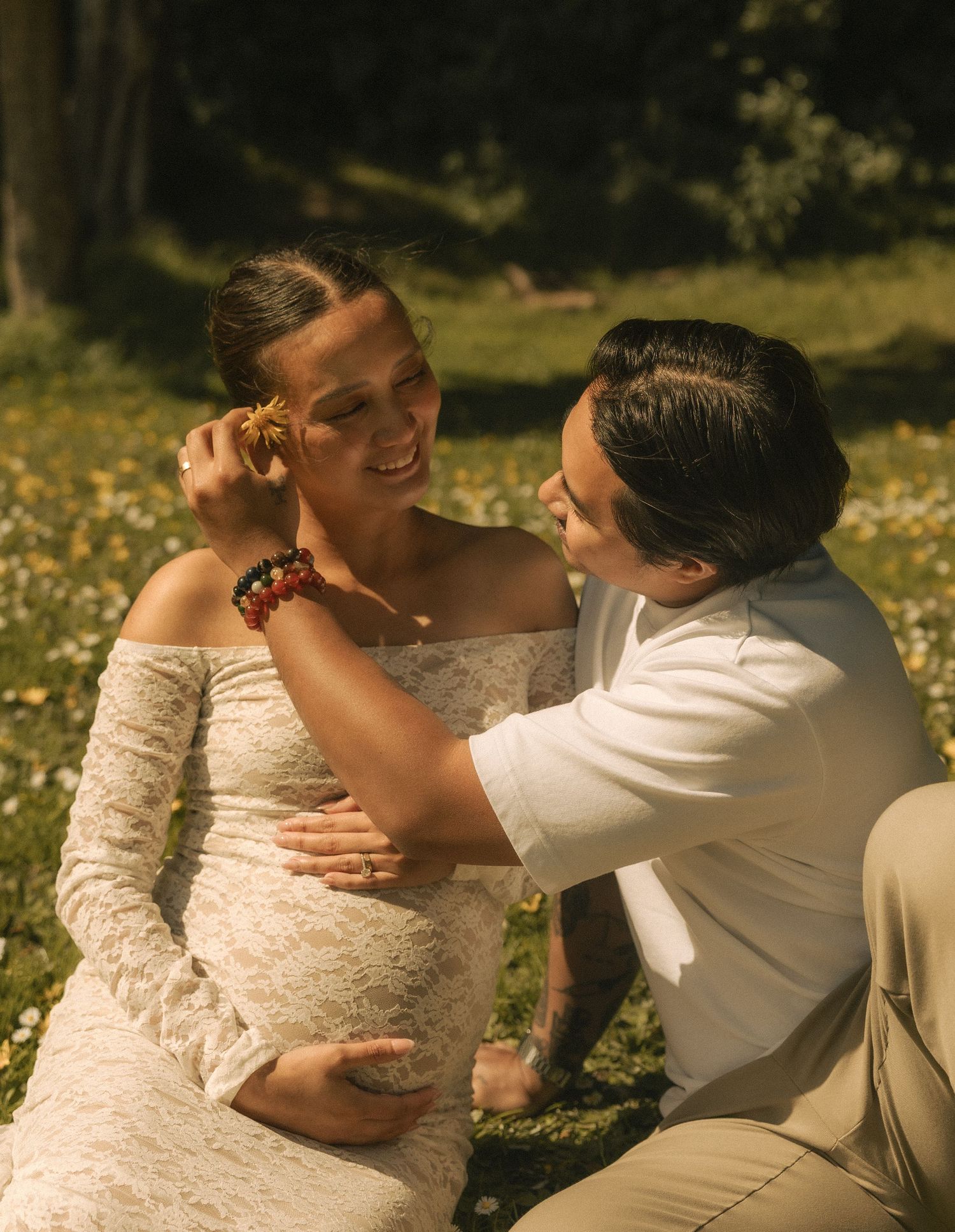 Couple in wedding attire sharing a tender moment outdoors, bride in white lace dress smiling as groom adjusts her earring.