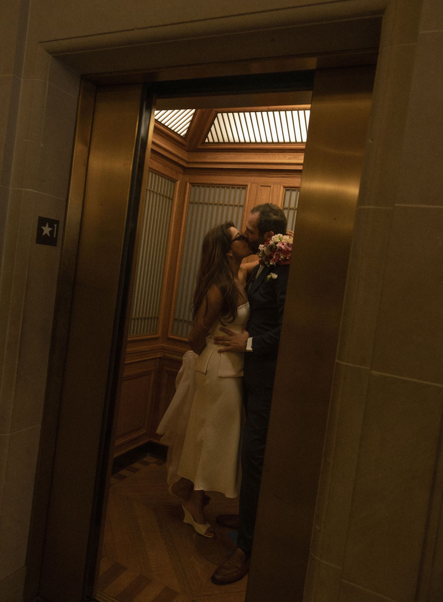 Bride and groom sharing a romantic kiss inside an elegant elevator on their wedding day.