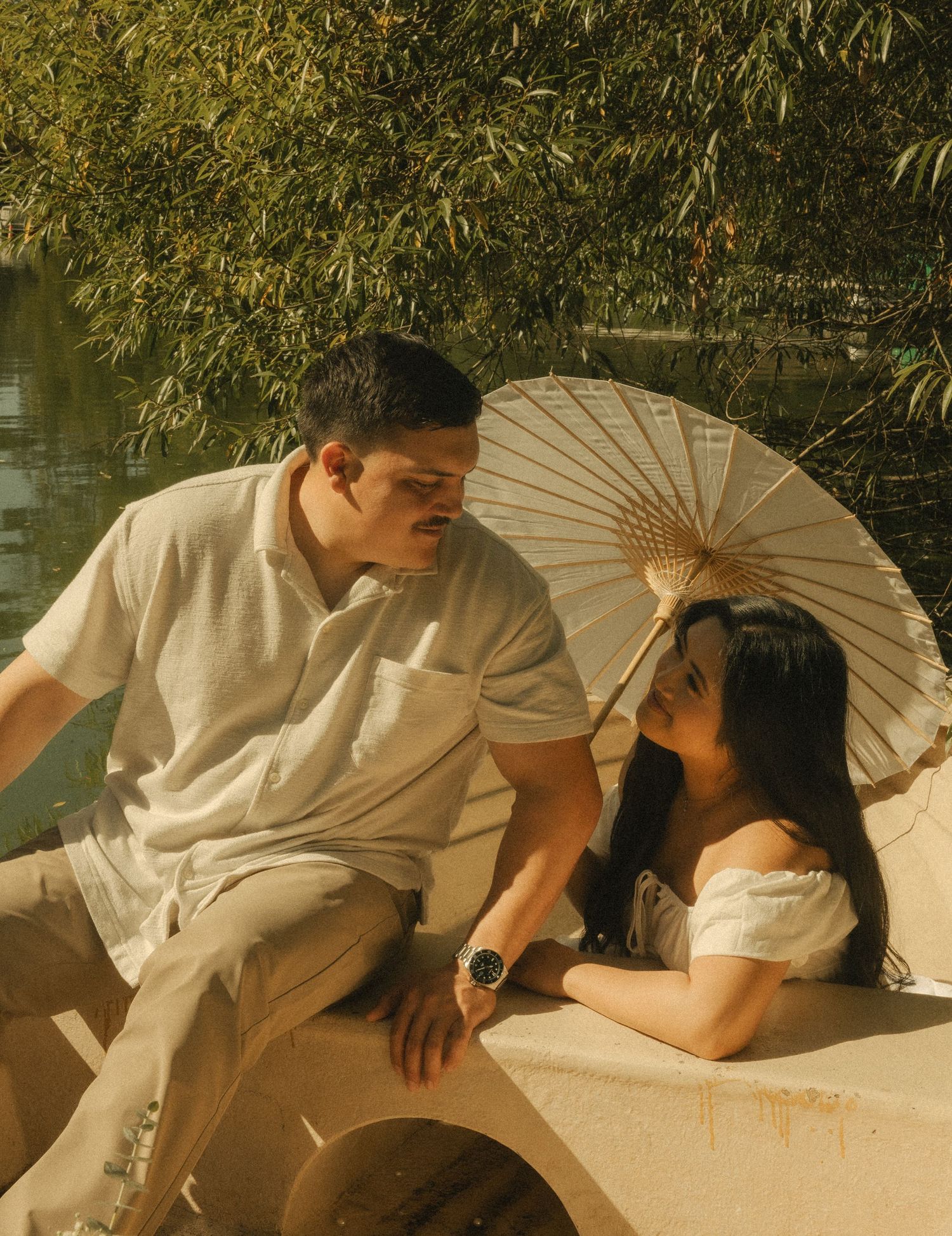 Couple sitting in a boat by a lake, sharing a romantic moment under a white paper parasol umbrella.