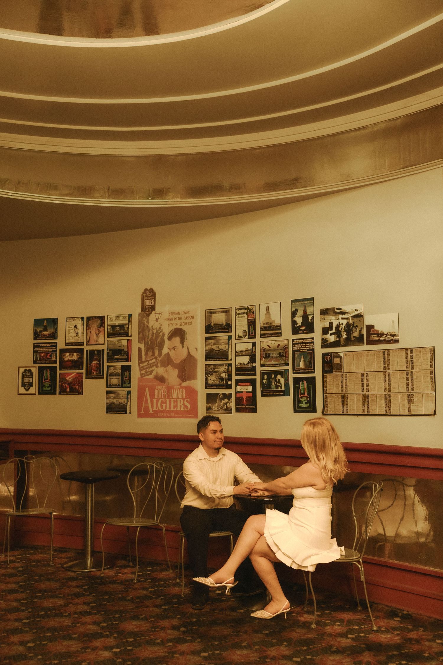 Couple holding hands at a vintage cinema lobby with classic movie posters on the wall.