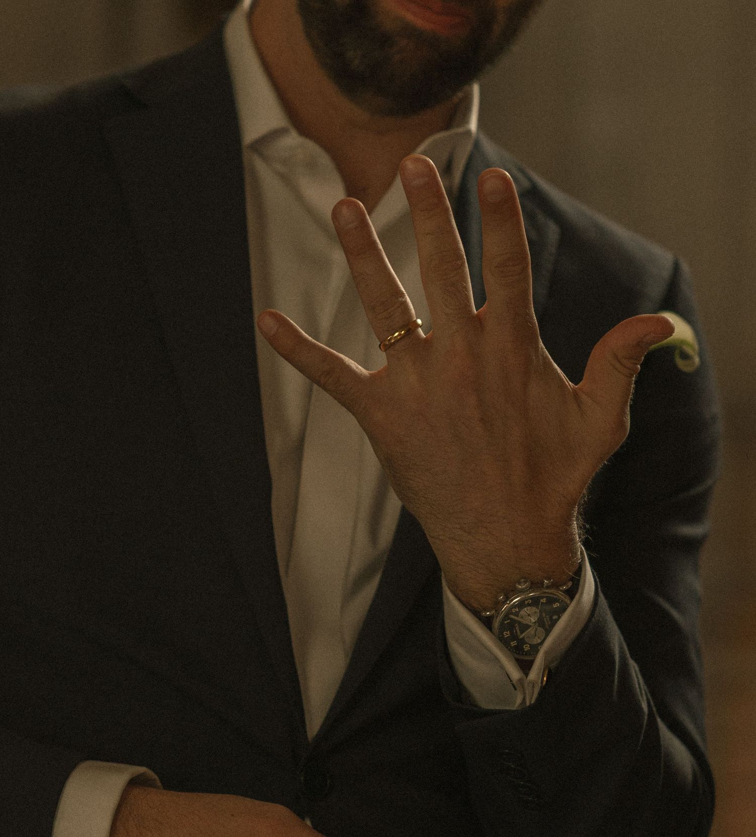 Man in dark suit displaying ring on hand with luxury watch, close-up shot.