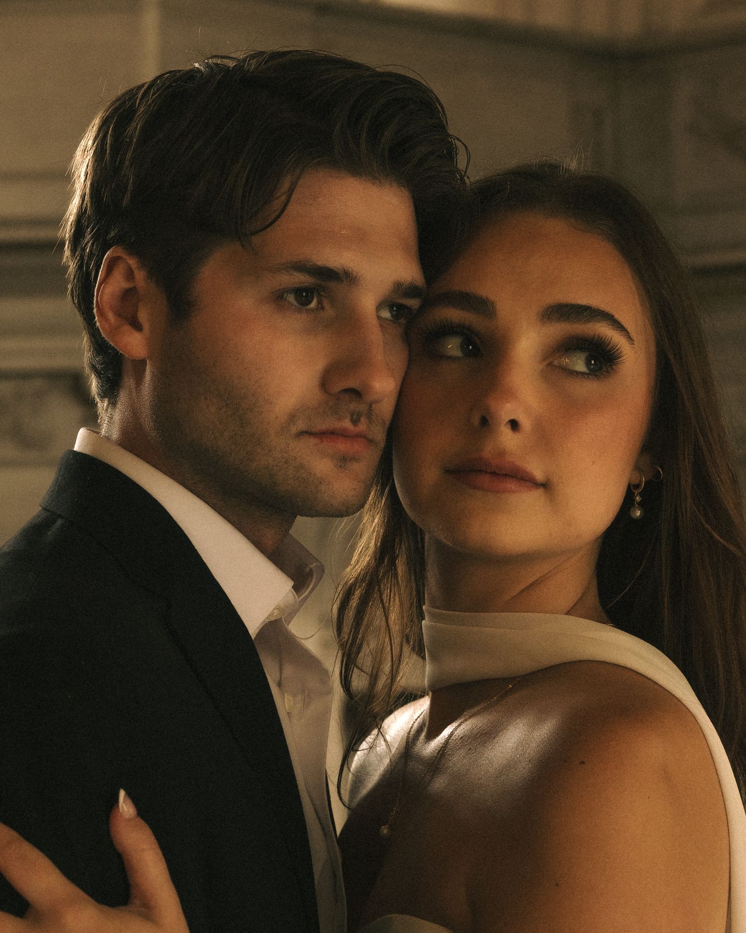 Elegant couple in formal attire posing intimately, man in black suit and woman in white dress.