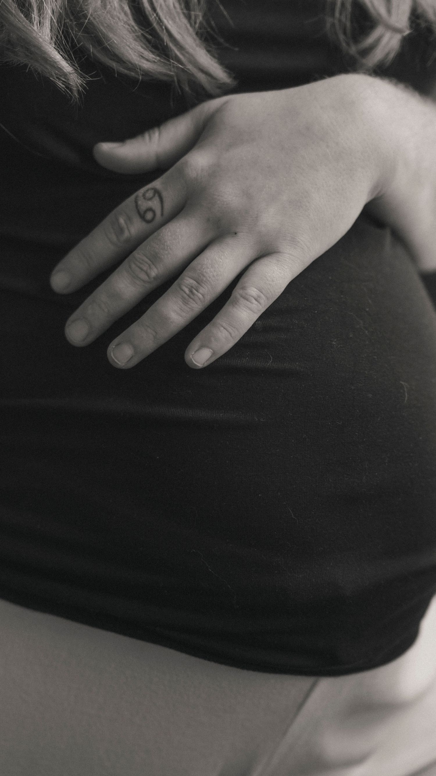 Hand som vilar mot gravid mage under en stillsam och dokumentär gravidfotografering