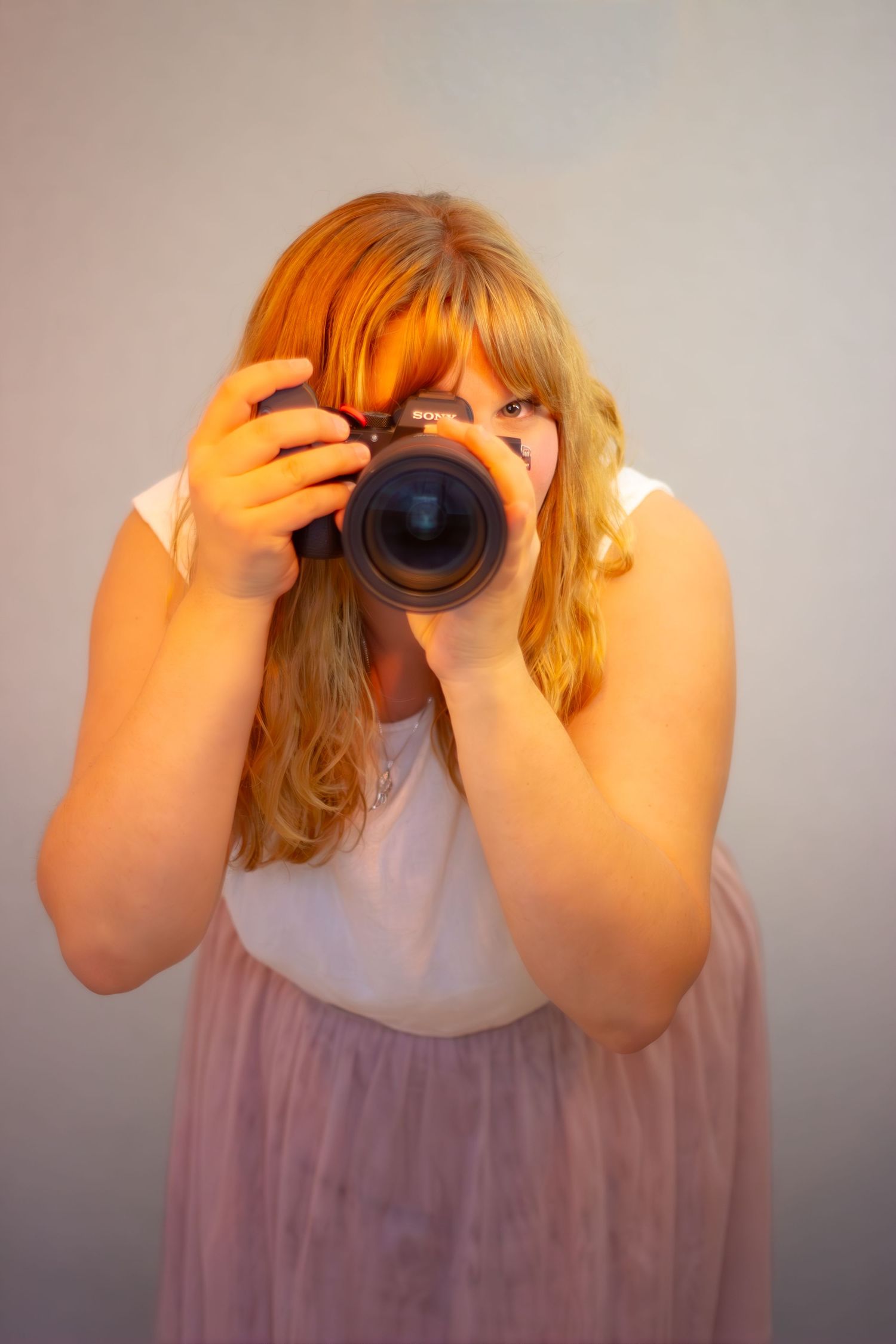 Dokumentär fotograf Isabelle Cordes håller en kamera framför ansiktet i mjukt naturligt ljus.
