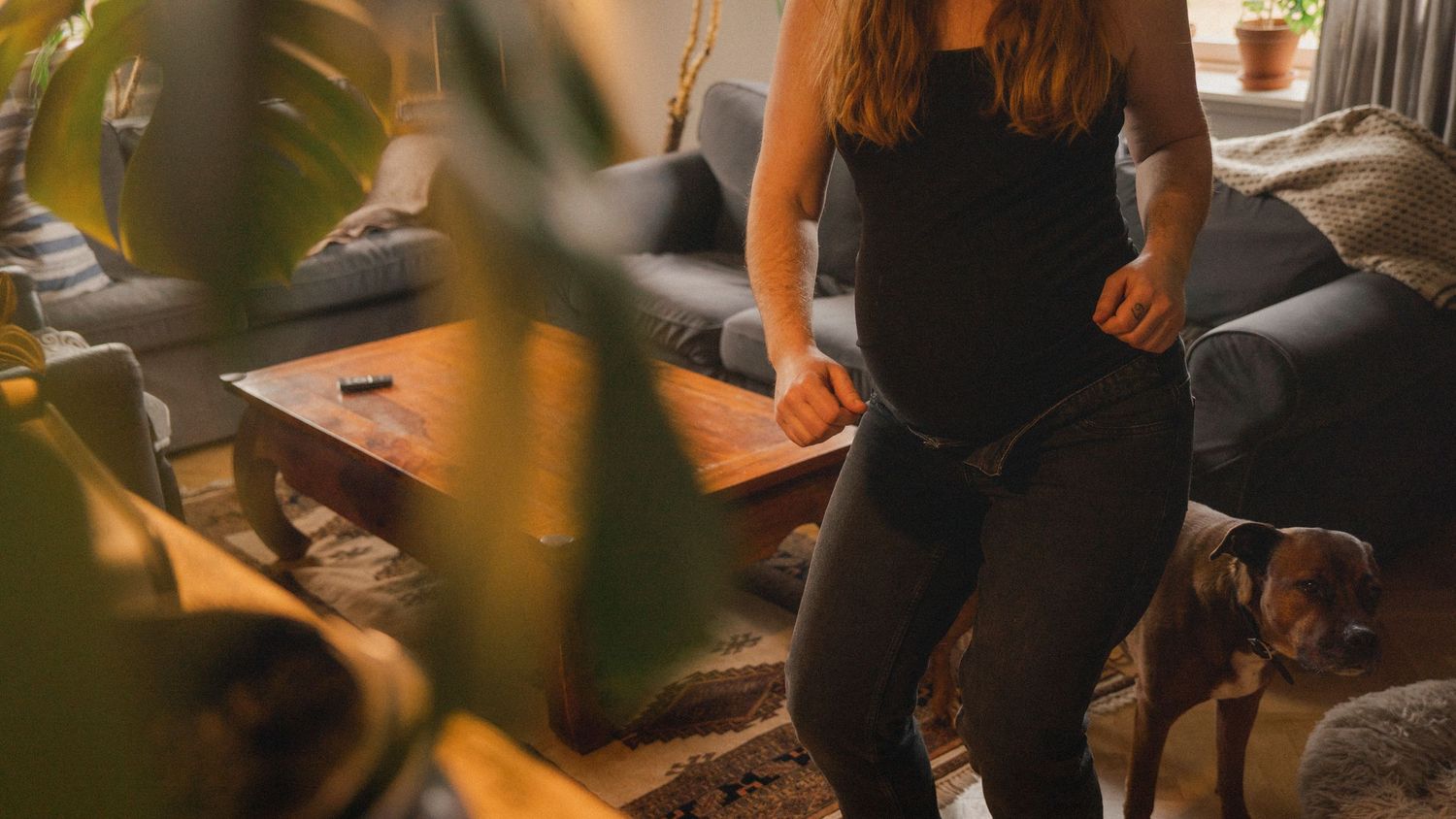 Gravid kvinna rör sig genom vardagsrummet i sitt hem under dokumentär gravidfotografering.
