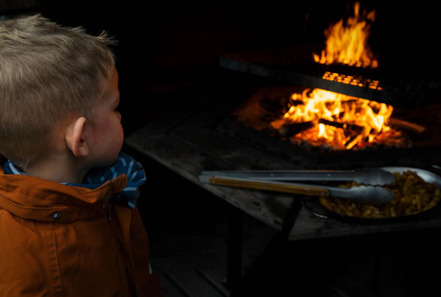 Barn tittar på matlagning över öppen eld utomhus.