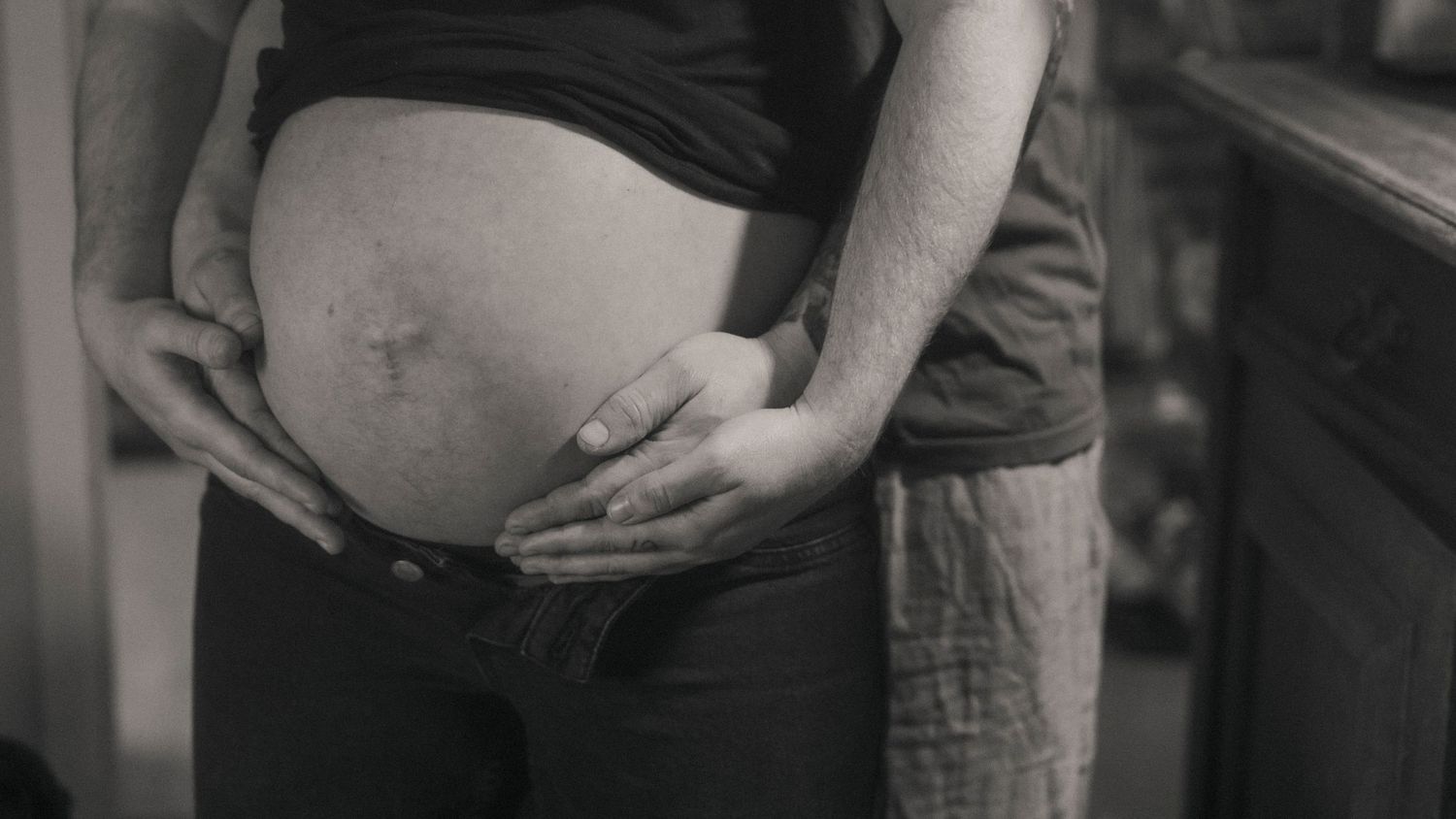 Blivande föräldrar tillsammans kring gravid mage i ett vardagligt ögonblick hemma.