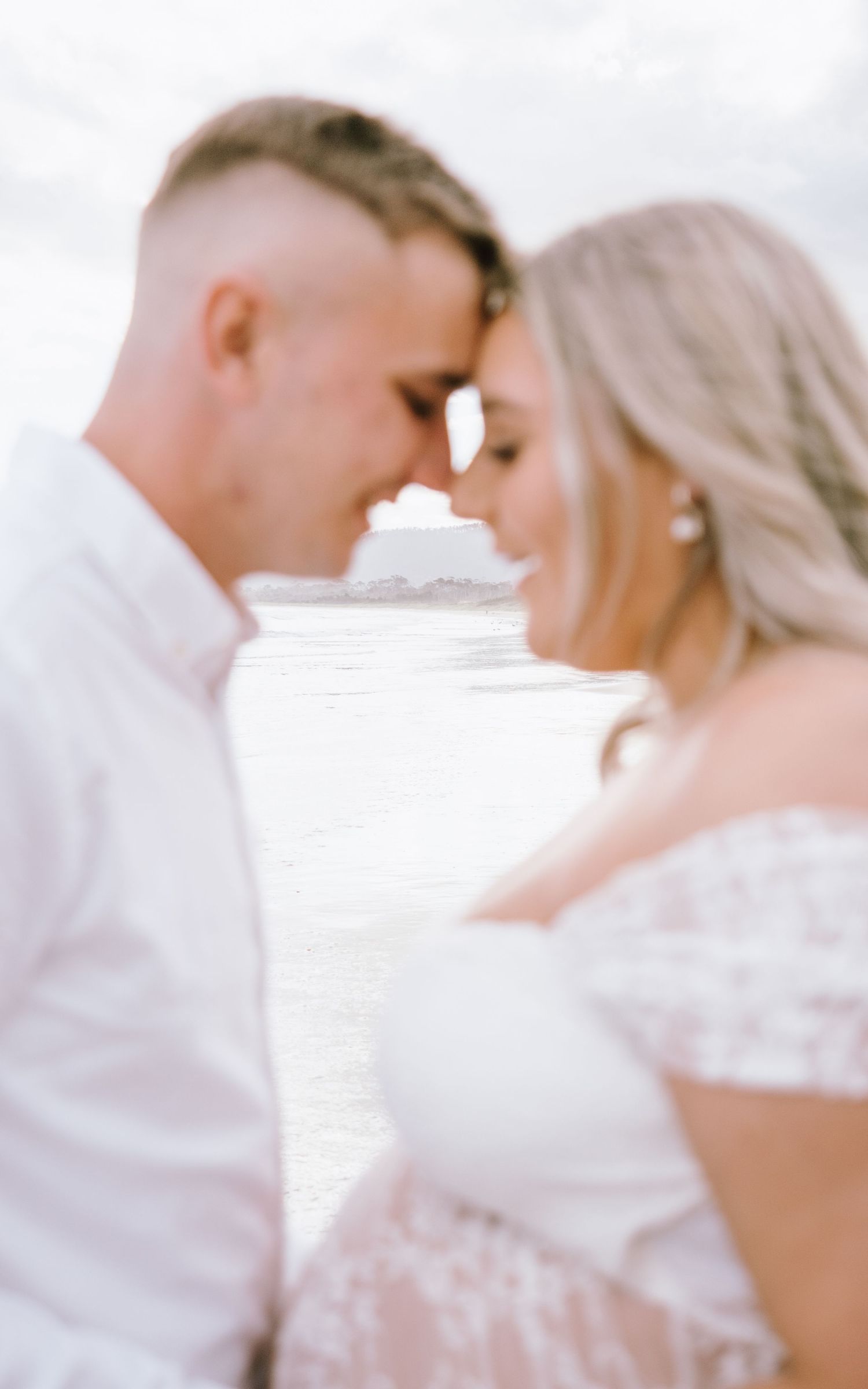 A romantic beach wedding couple shares an intimate moment at sunset in white attire.