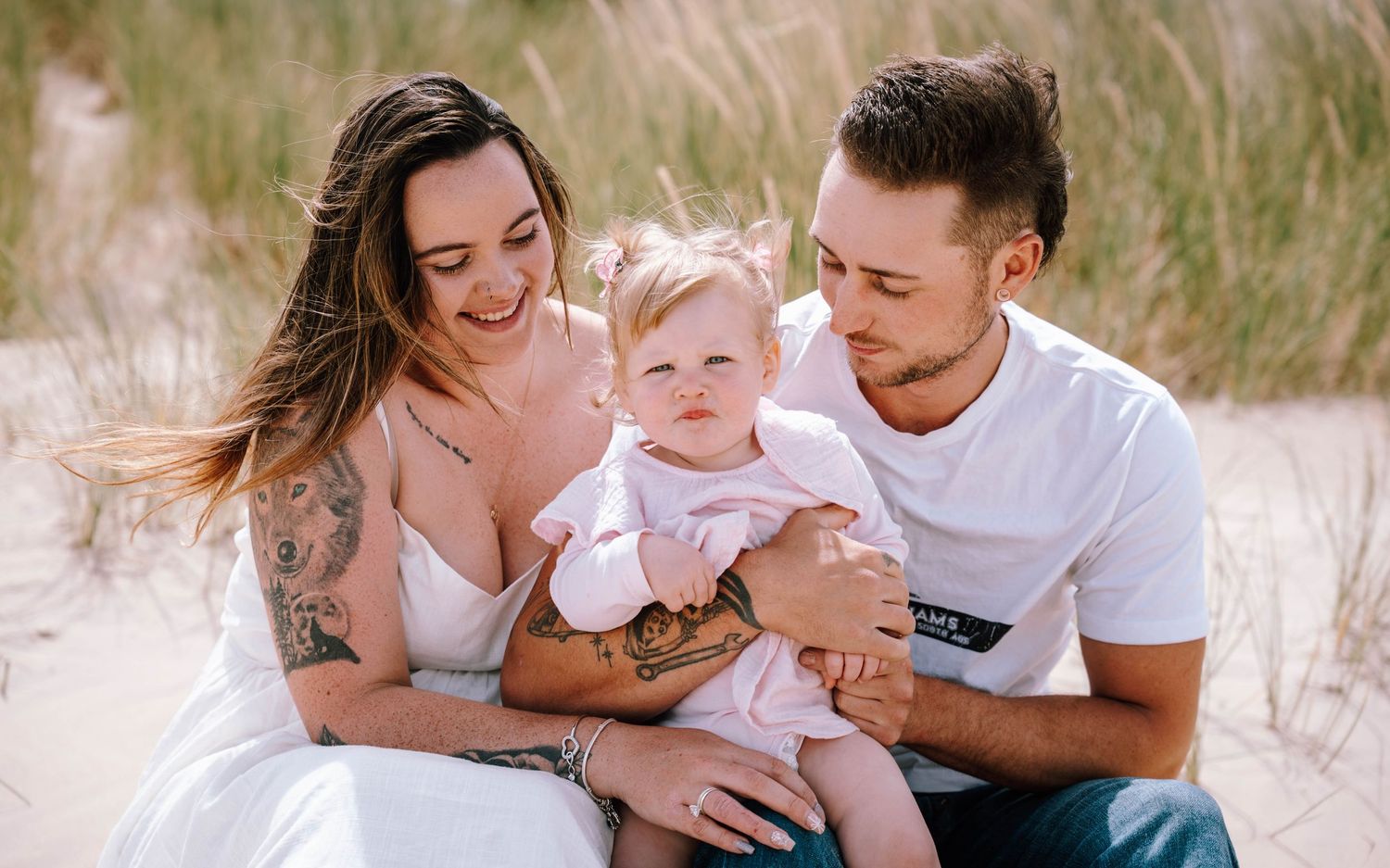 Sweet family moment captured on a grassy beach dune in soft natural light.