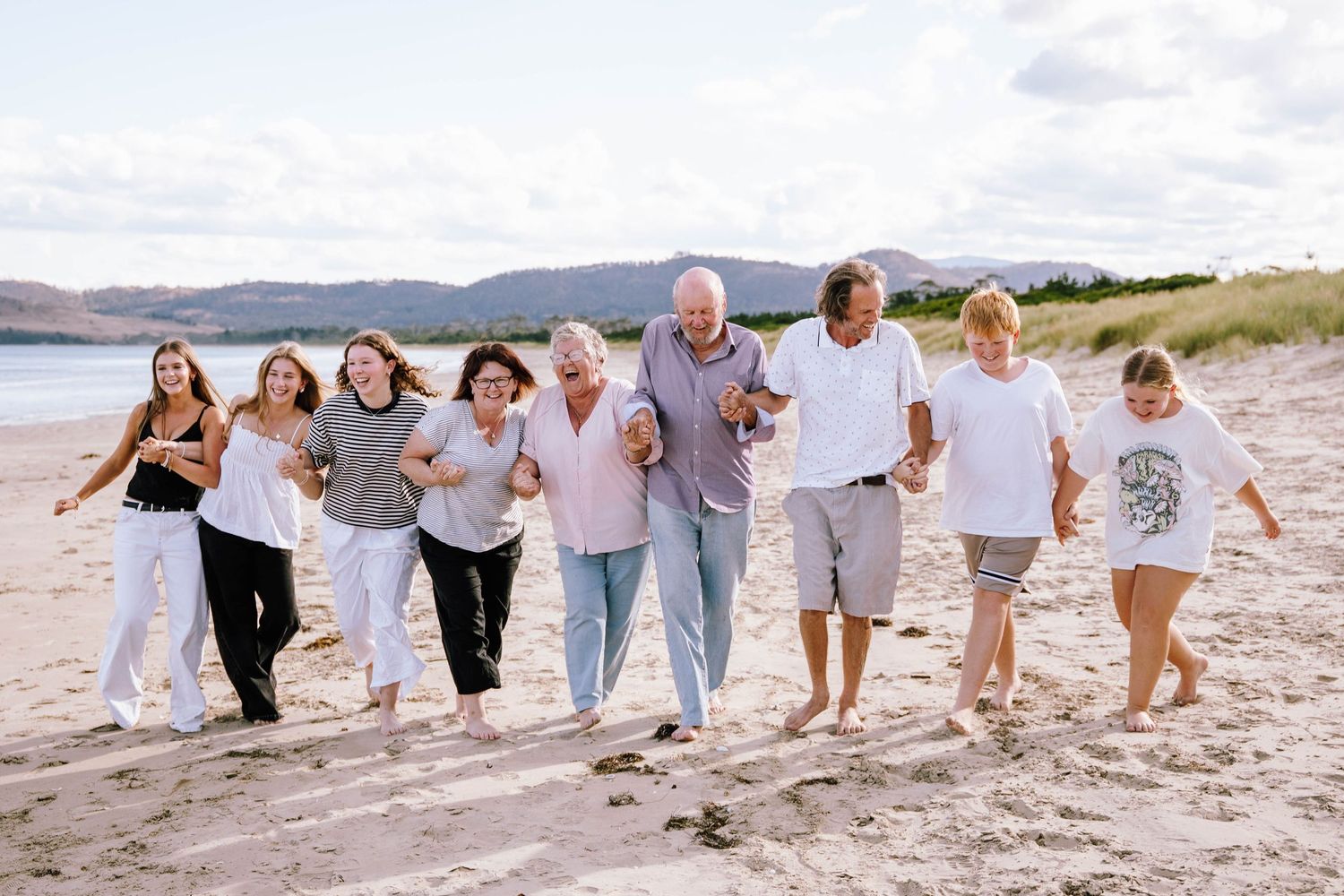 A group wearing white and beige outfits walks together in a line along a sandy beach at sunset.