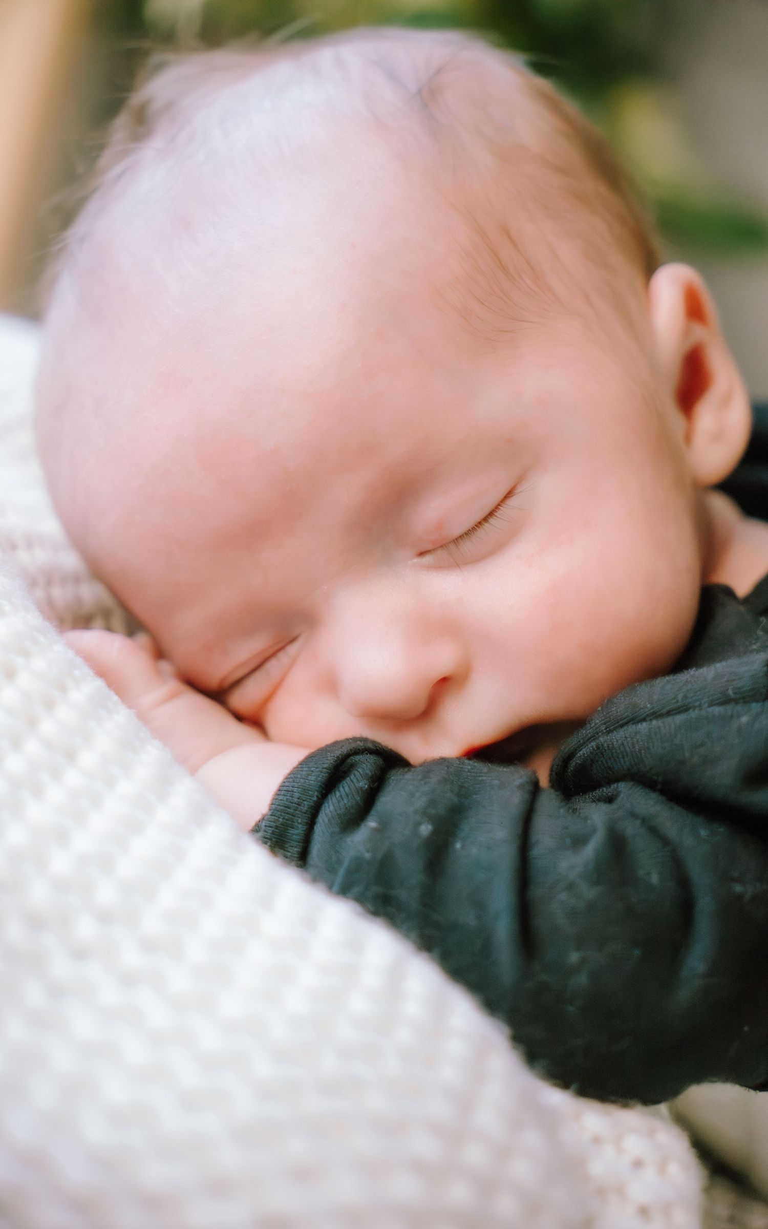 A peaceful sleeping baby rests on white textured bedding while wearing a dark colored outfit.