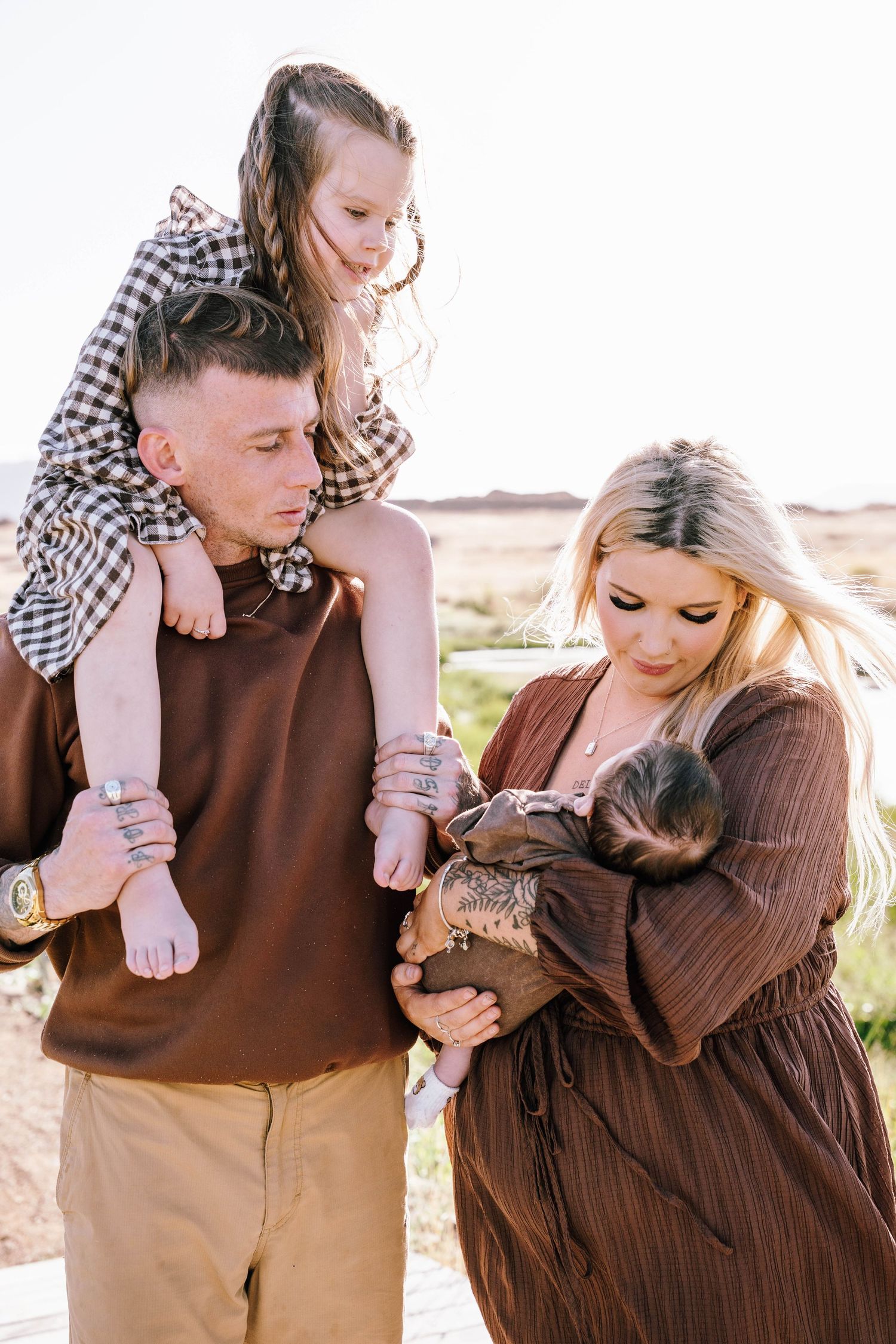 A family poses together outdoors in coordinating brown outfits against a natural desert landscape.
