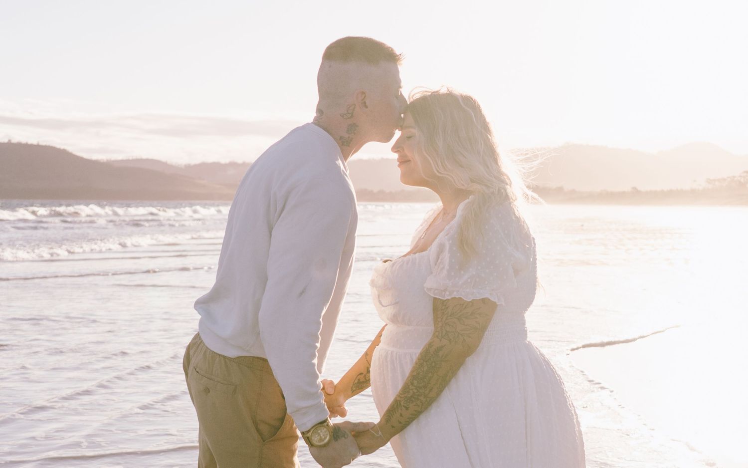 A couple walks hand in hand along a scenic beach at sunset with ocean waves rolling in.