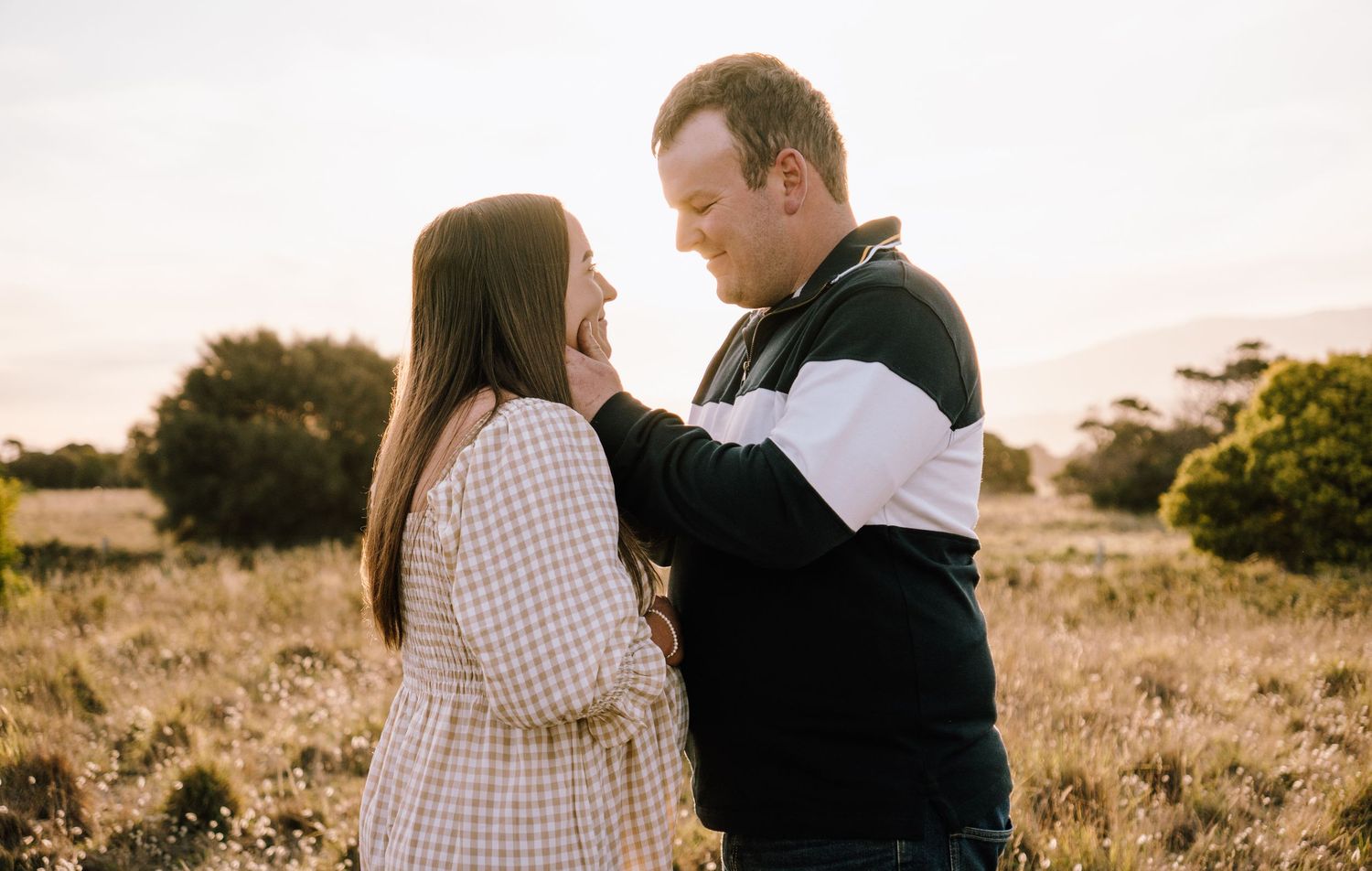 Couple embracing in a sunlit field during golden hour.
