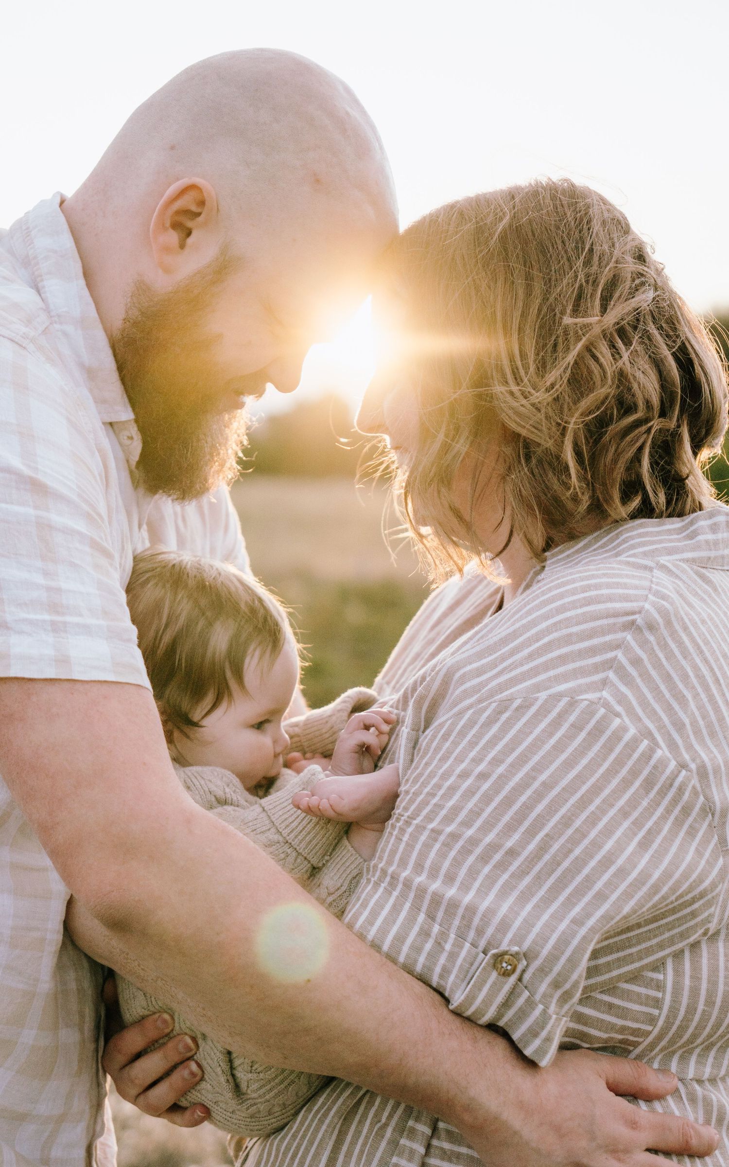 A loving family embraces in a golden sunset while wearing casual striped clothing and sharing tender moments together.