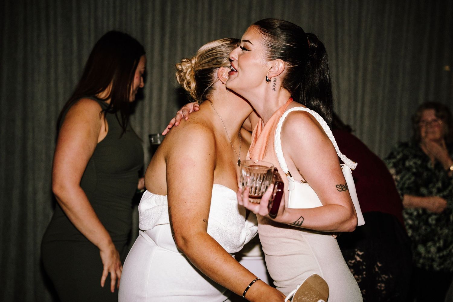 Bride sharing a joyful kiss on the cheek with a guest at wedding reception.