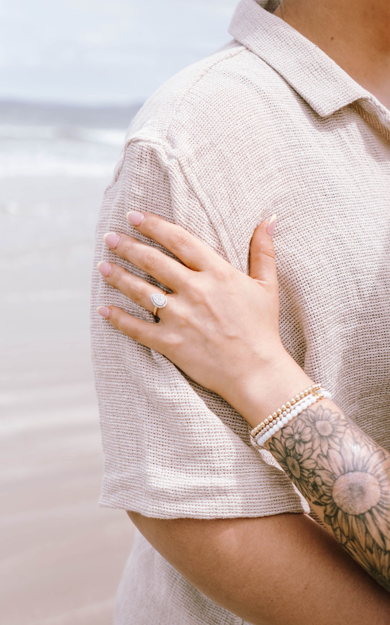 Close-up of hands wearing pearl bracelet and showing floral tattoo sleeve against light colored top.