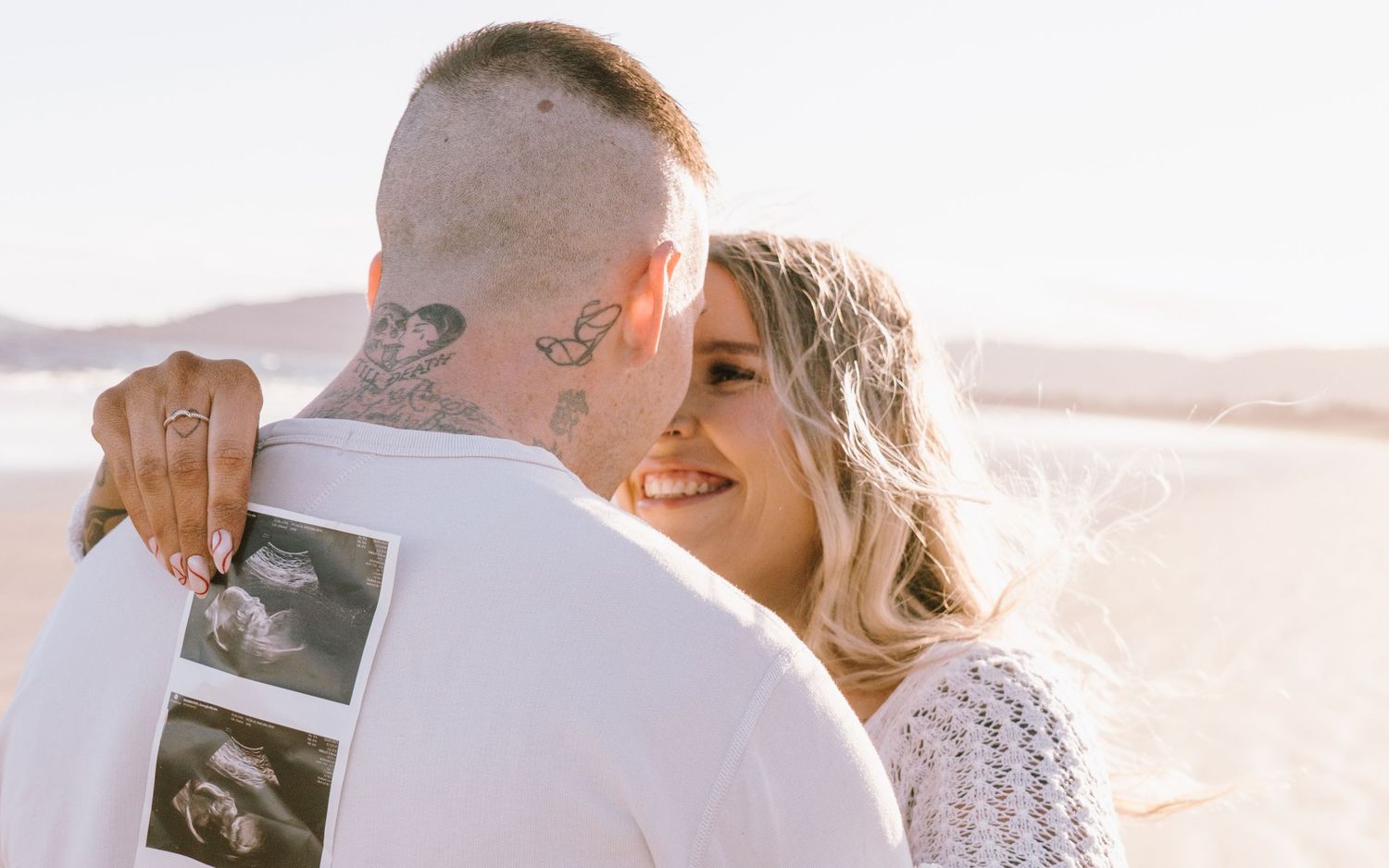 Couple sharing intimate moments of their pregnancy announcement on beach during golden hour photoshoot.