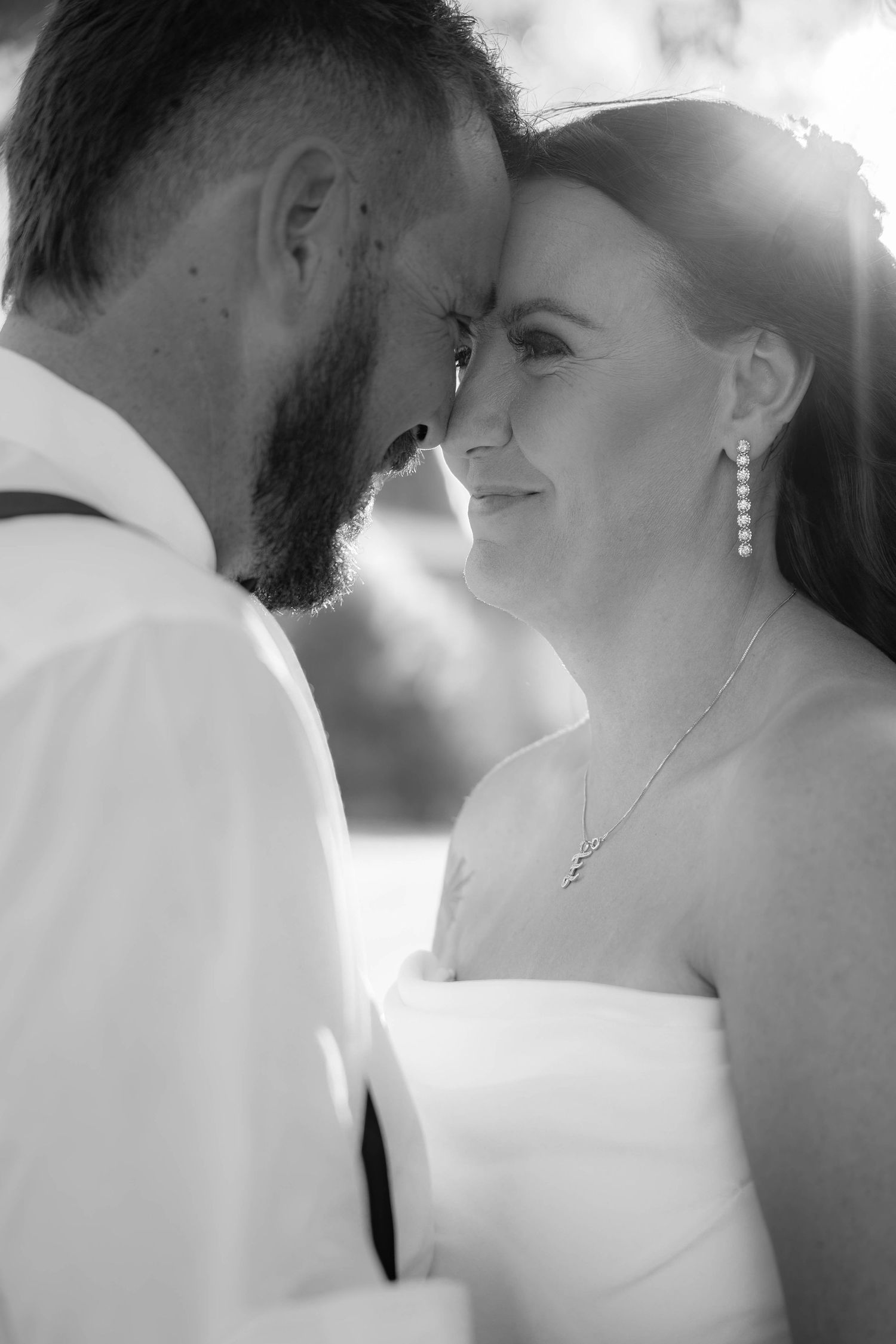 Black and white wedding photo of smiling bride and bearded groom touching foreheads in a romantic intimate moment.