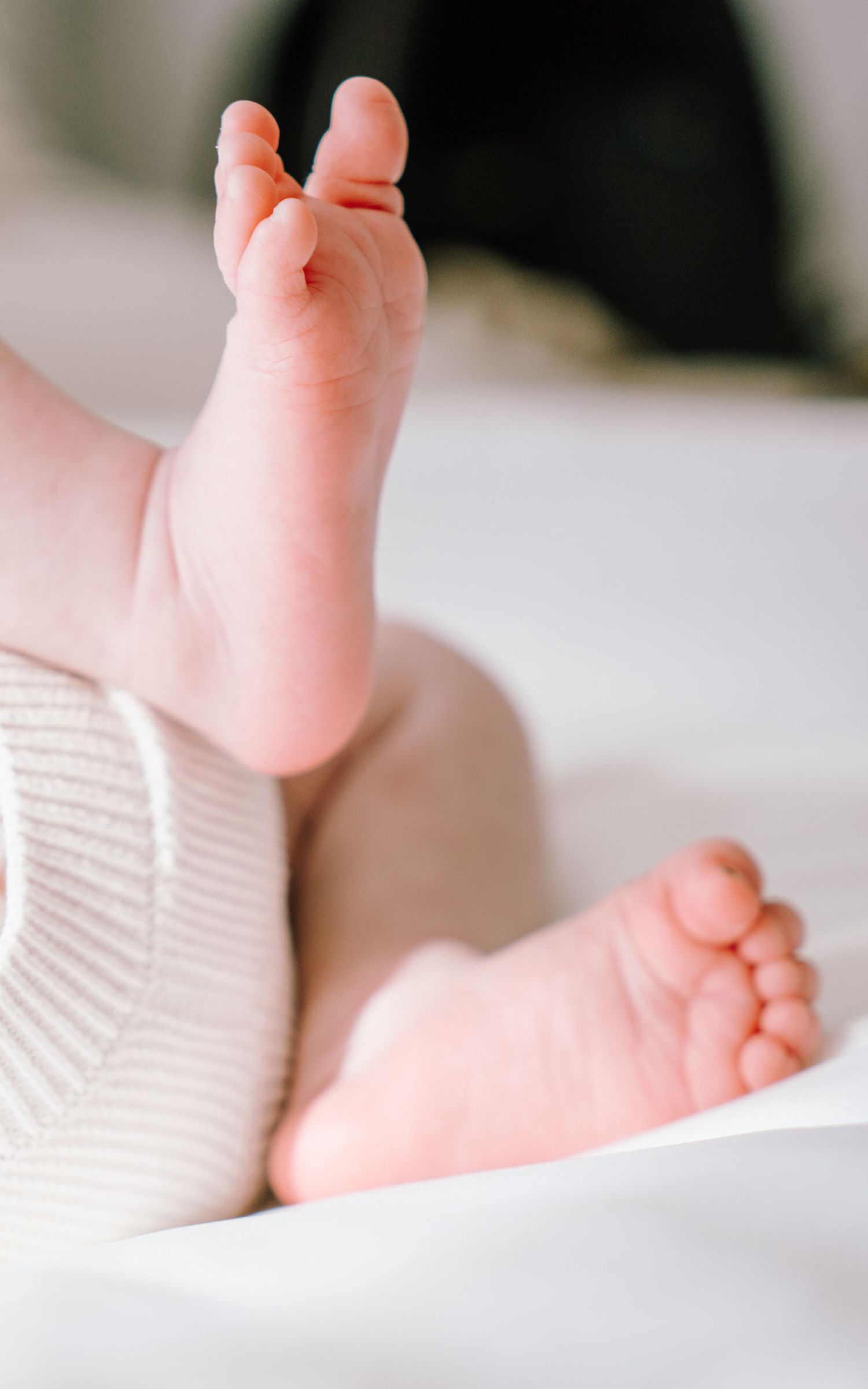 Close-up view of tiny baby feet against white bedding, showing delicate toes and soft pink skin.