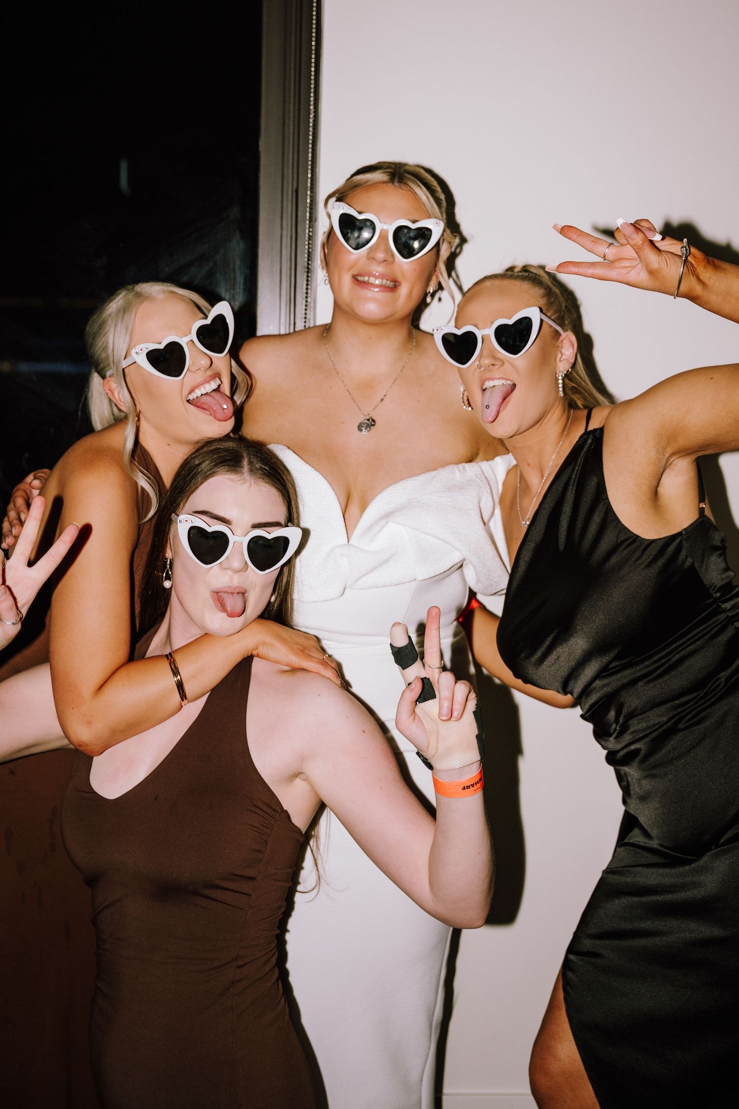 Bride and bridesmaids in heart sunglasses posing playfully at a wedding reception.