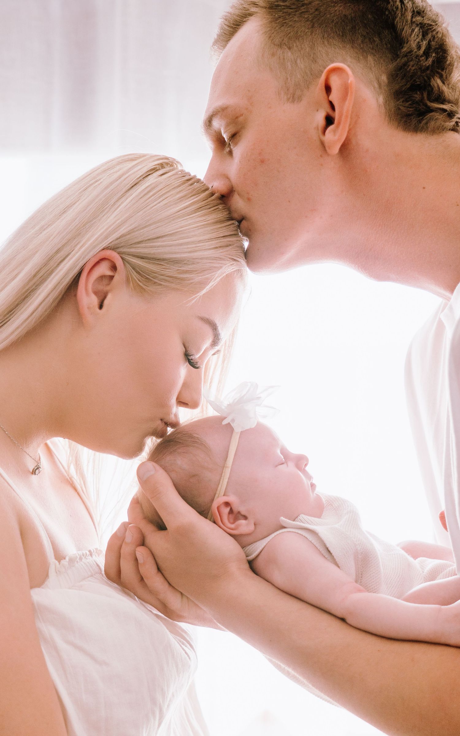 Tender moments captured in a series of soft-lit photos showing parent and baby bonding in white attire.