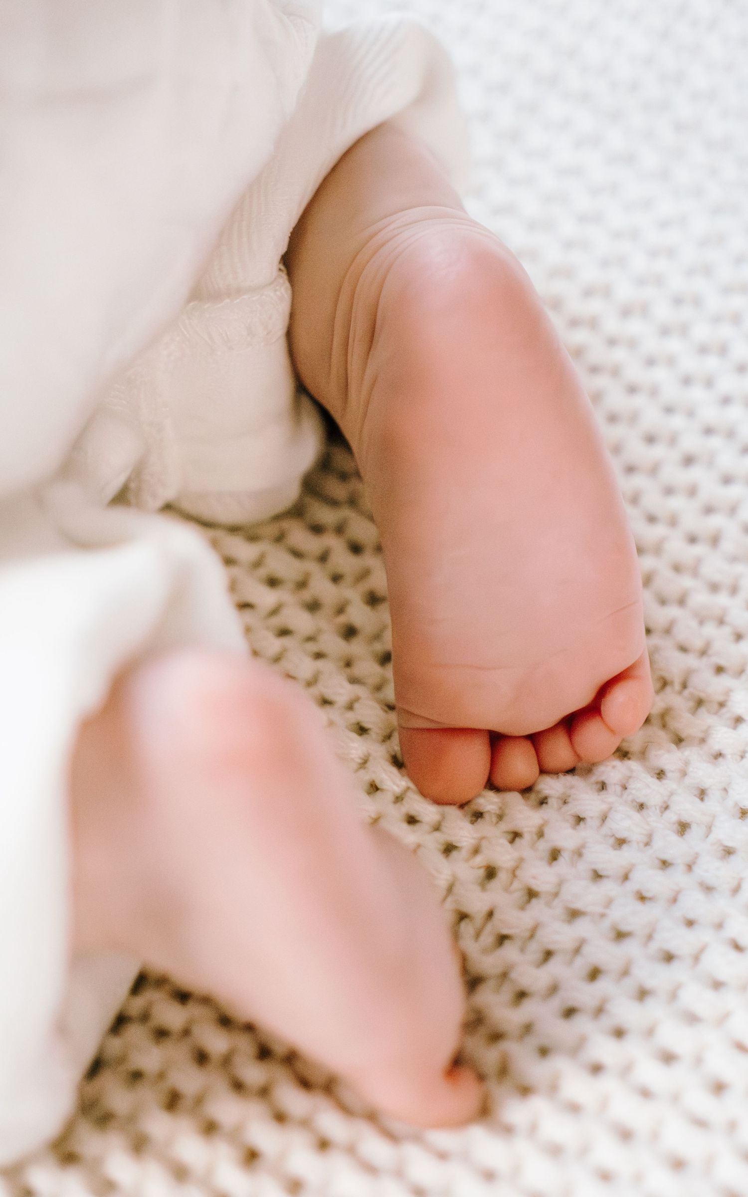 Close-up of tiny baby feet on a white knitted blanket showing delicate toes and soft skin.