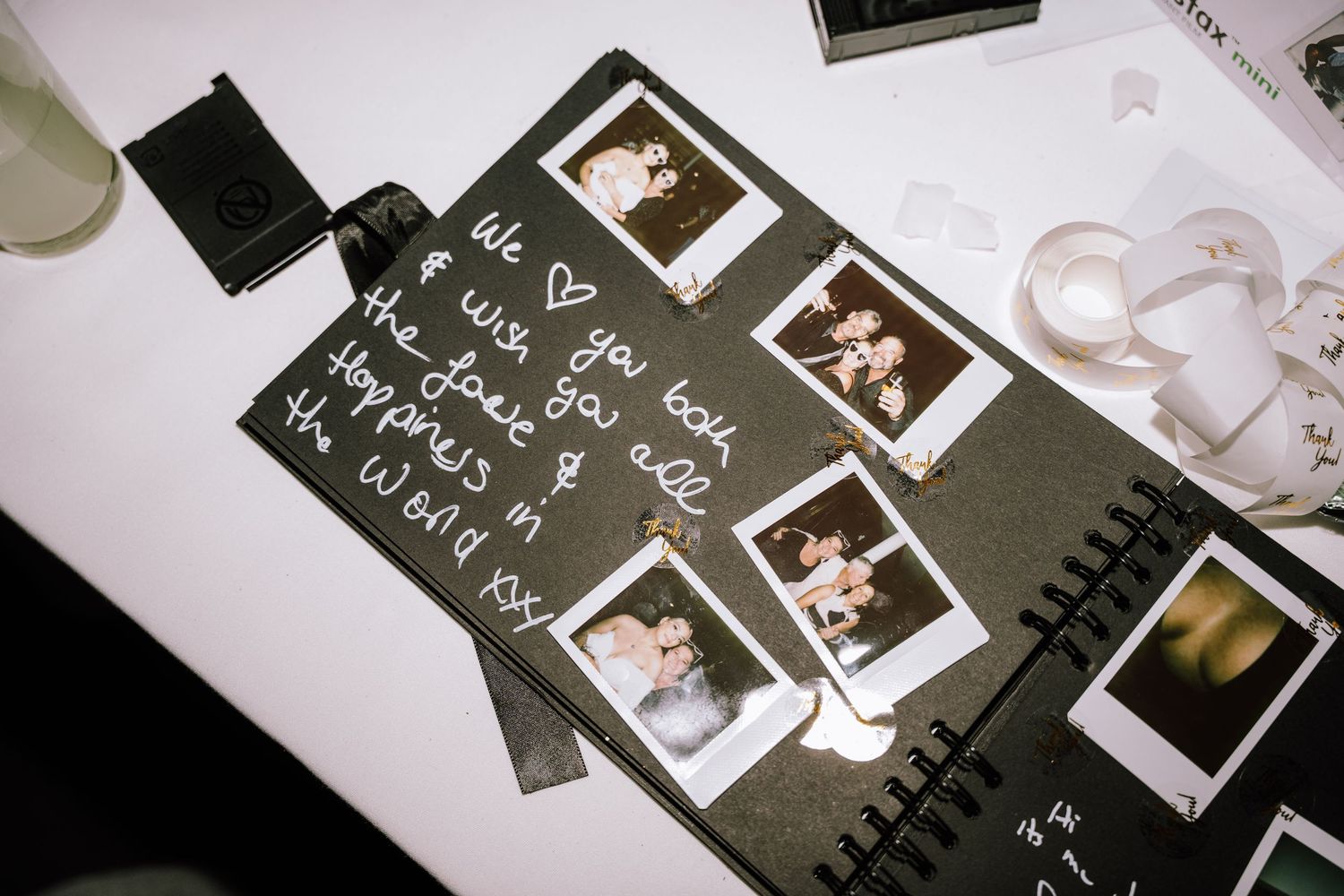 Polaroid photo guestbook with handwritten wedding wishes on a black scrapbook page.