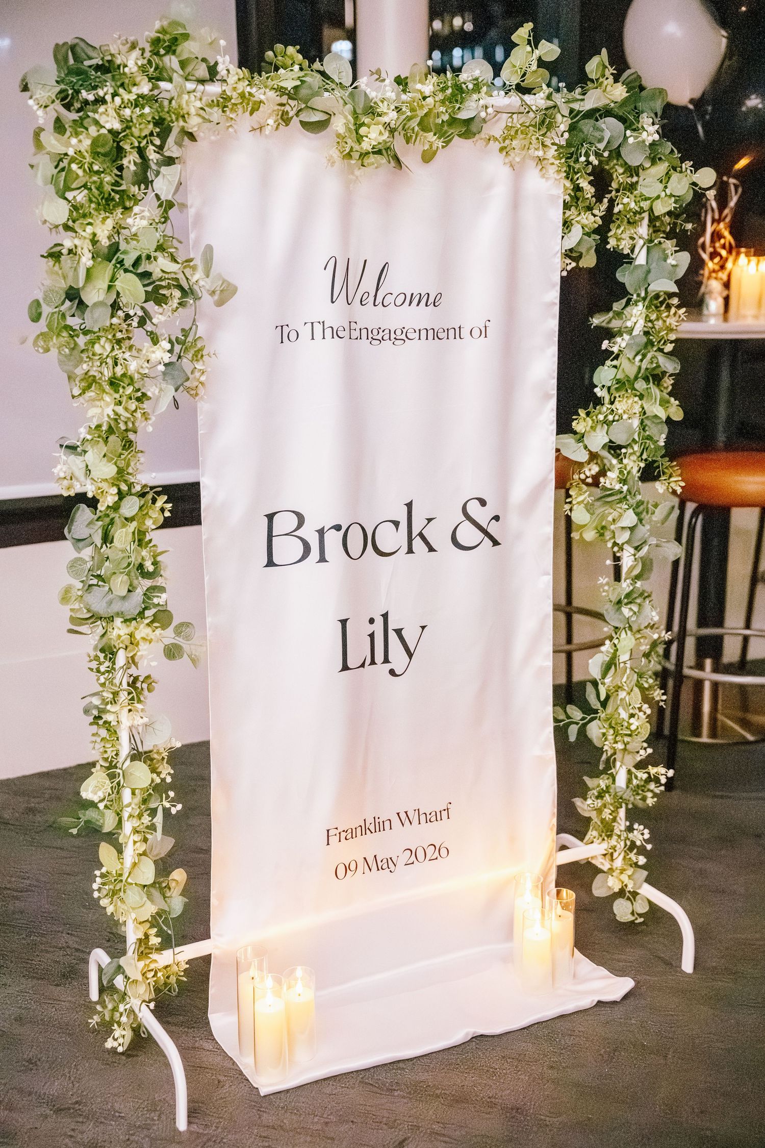 Elegant engagement party welcome sign for Brock and Lily at Franklin Wharf, adorned with greenery and candles.