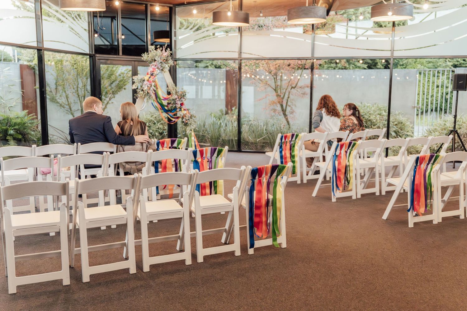 White folding chairs with colorful ribbon decorations set up for an indoor wedding ceremony venue.