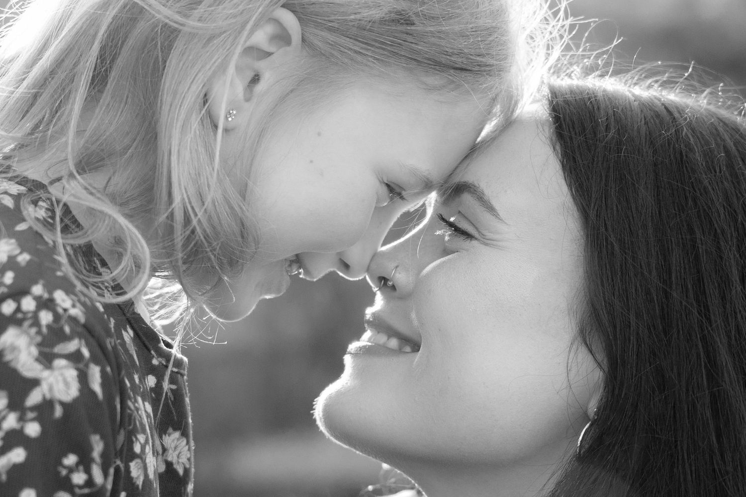 Black and white photo of a mother and young daughter smiling and touching foreheads in a tender moment.