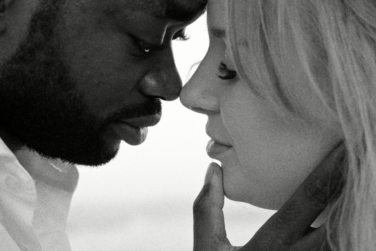 Black and white photo of a man and woman in an intimate close face-to-face moment, almost touching noses.