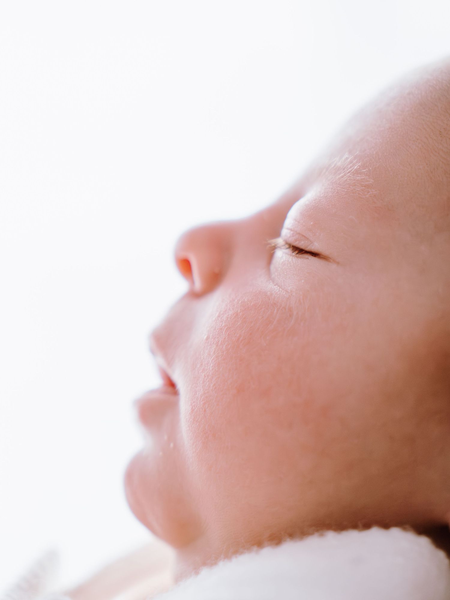Close-up profile of a sleeping newborn baby with soft skin and delicate features against a white background.