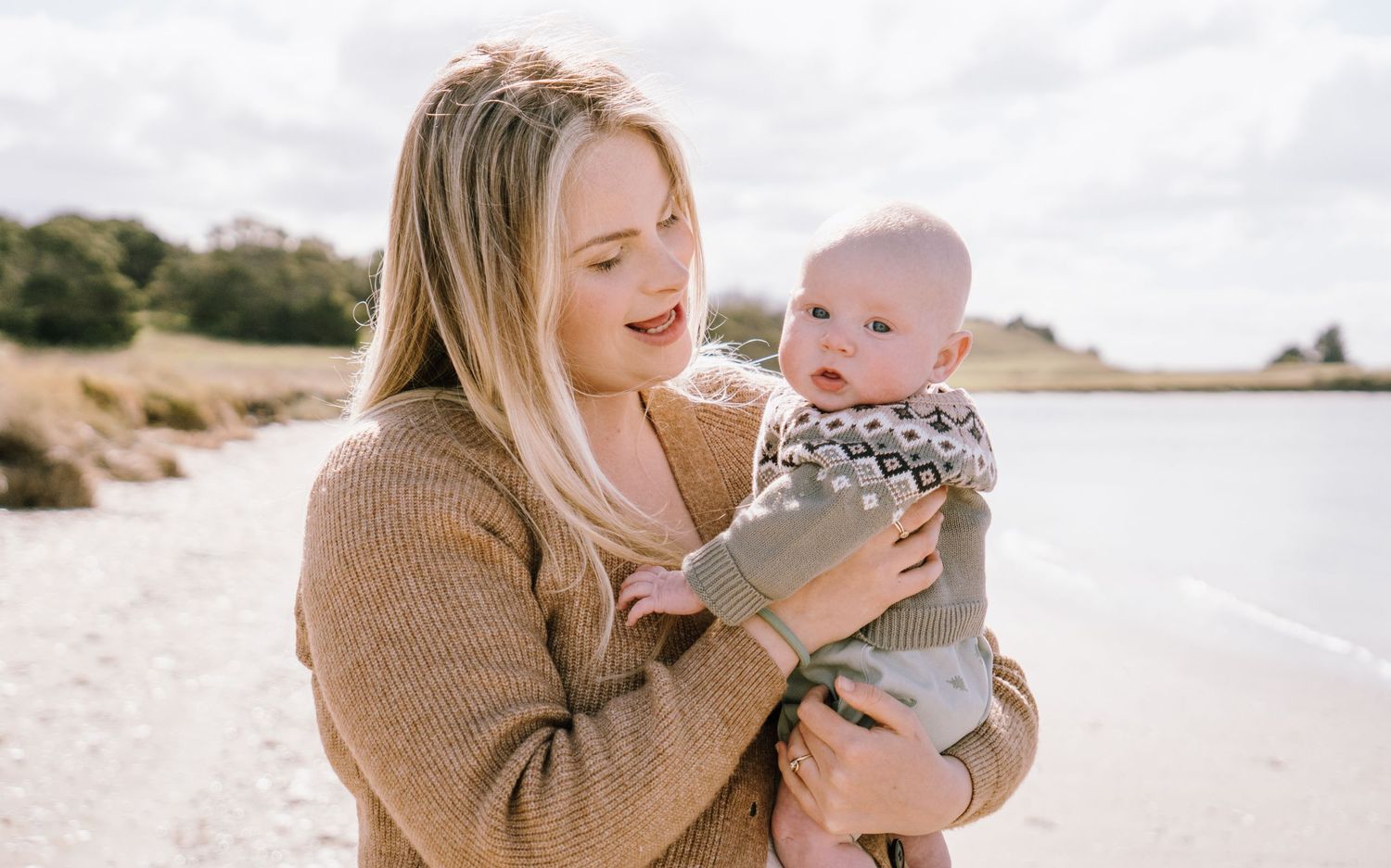 Mother and baby sharing joyful moments on a sunny beach.