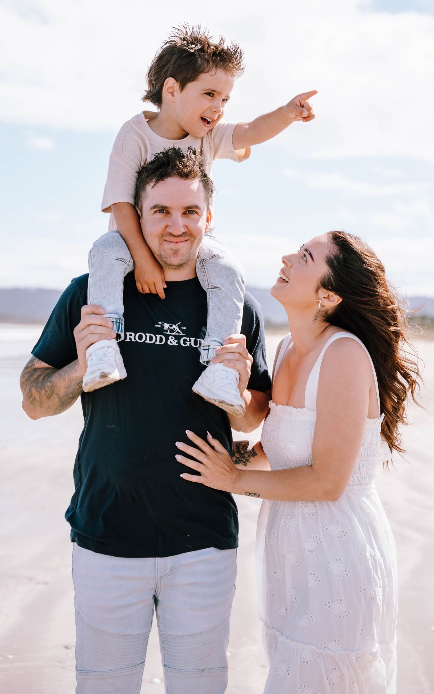 Family enjoying playful moments together on a bright sunny beach in casual summer attire.