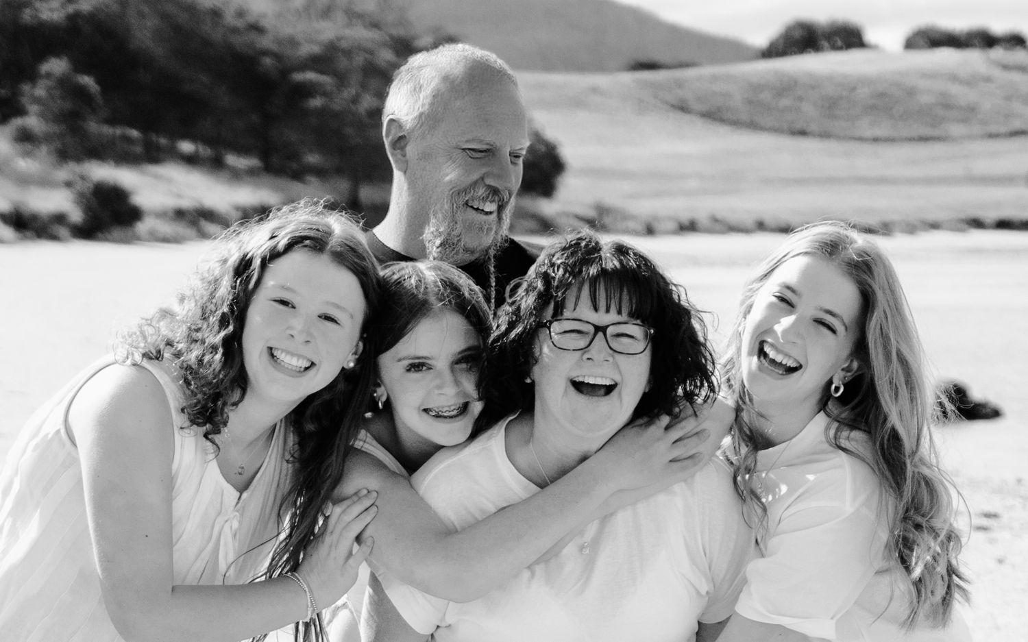 Black and white photo of a happy family of five smiling and embracing on a beach.