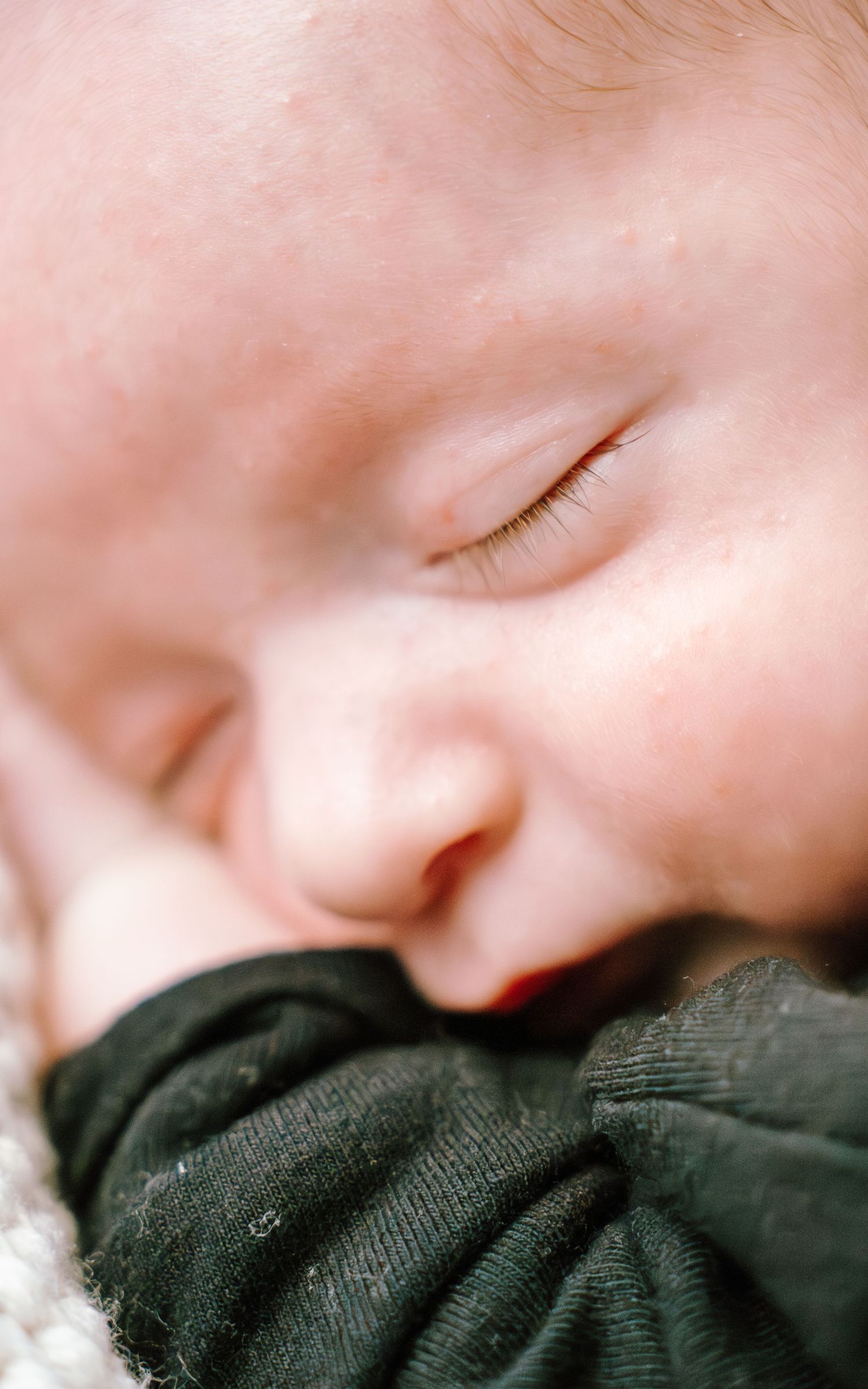 Close-up image of a sleeping infant resting on dark fabric with soft pink lighting.
