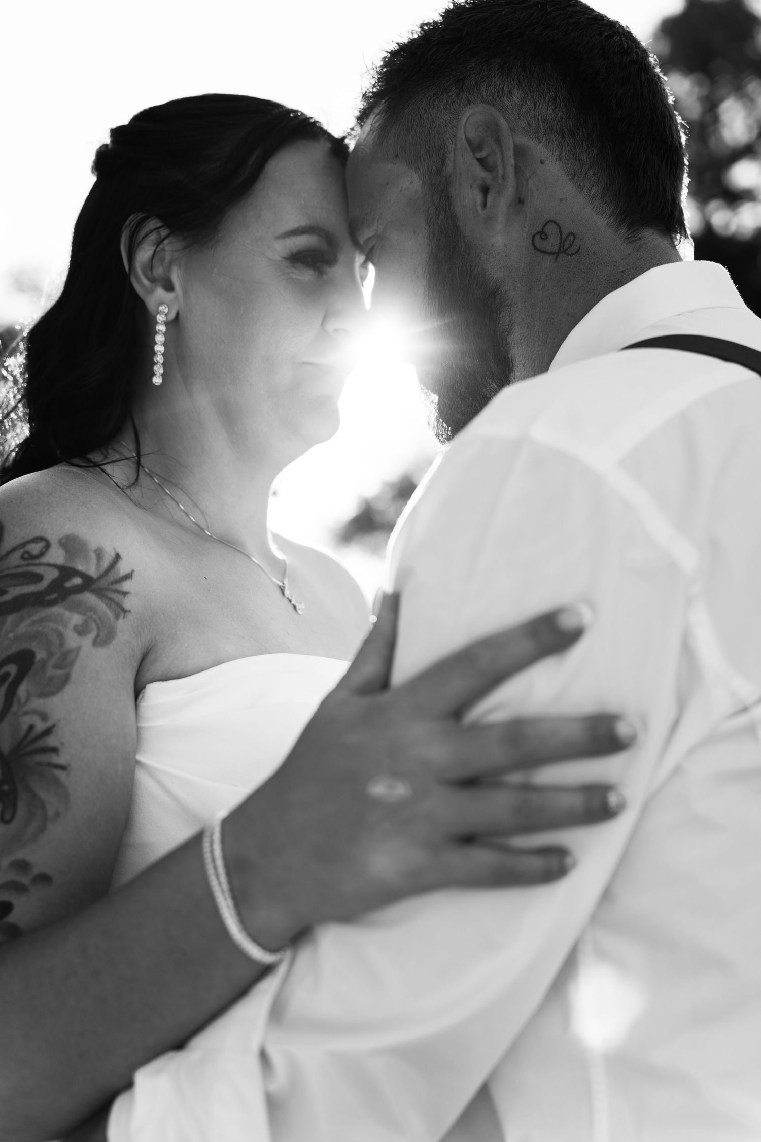 Black and white wedding photo of tattooed bride and groom sharing an intimate moment with sun flare between them.