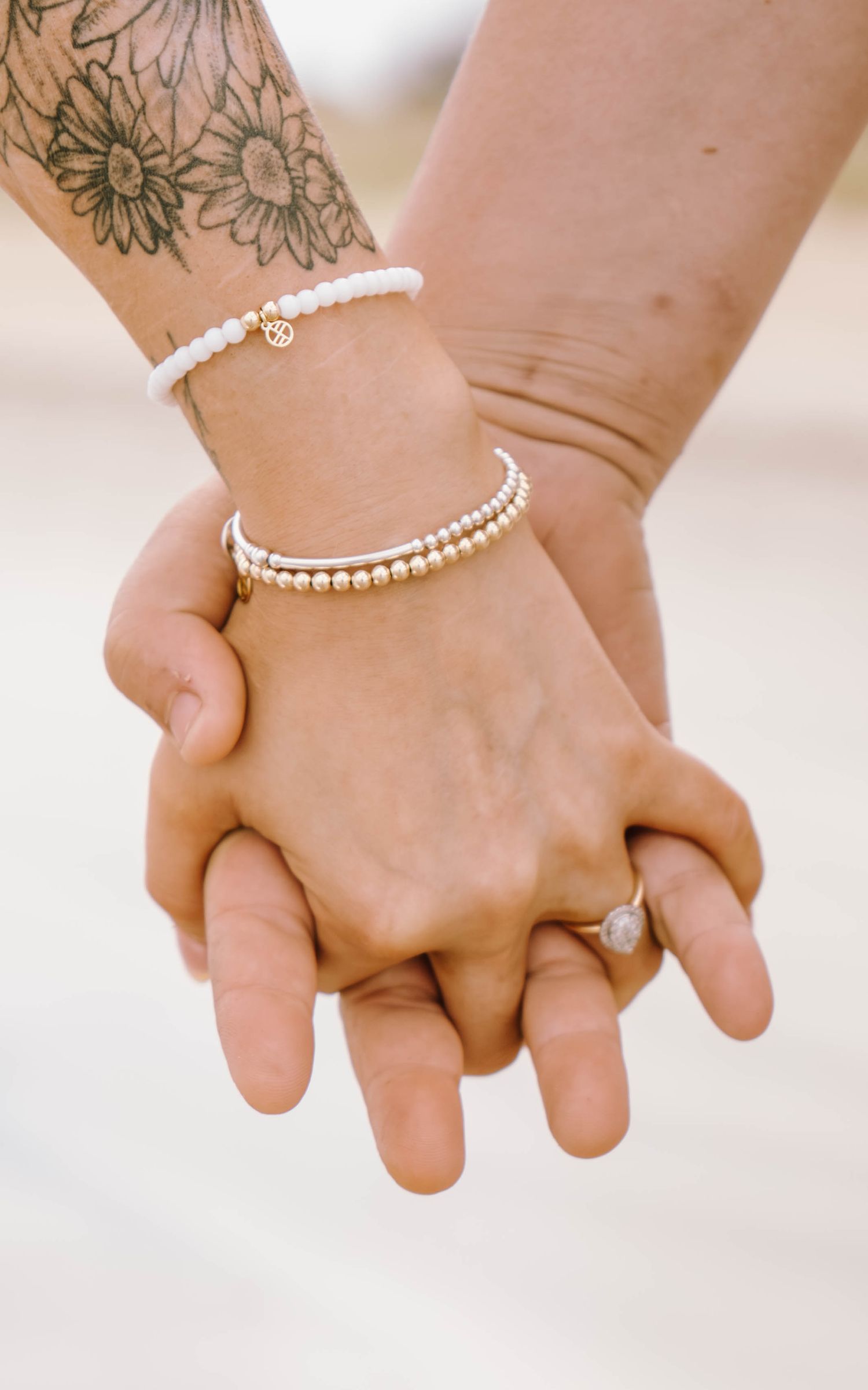 Close-up of hands wearing delicate beaded bracelets and a diamond ring against a light background.
