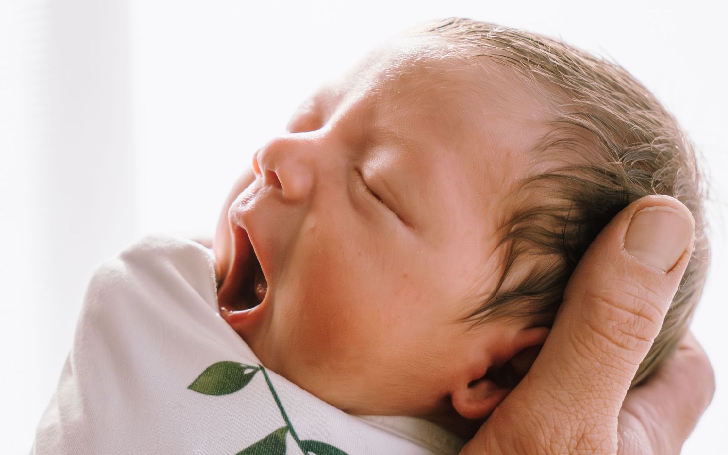 A newborn baby sleeps peacefully while being cradled in gentle hands.
