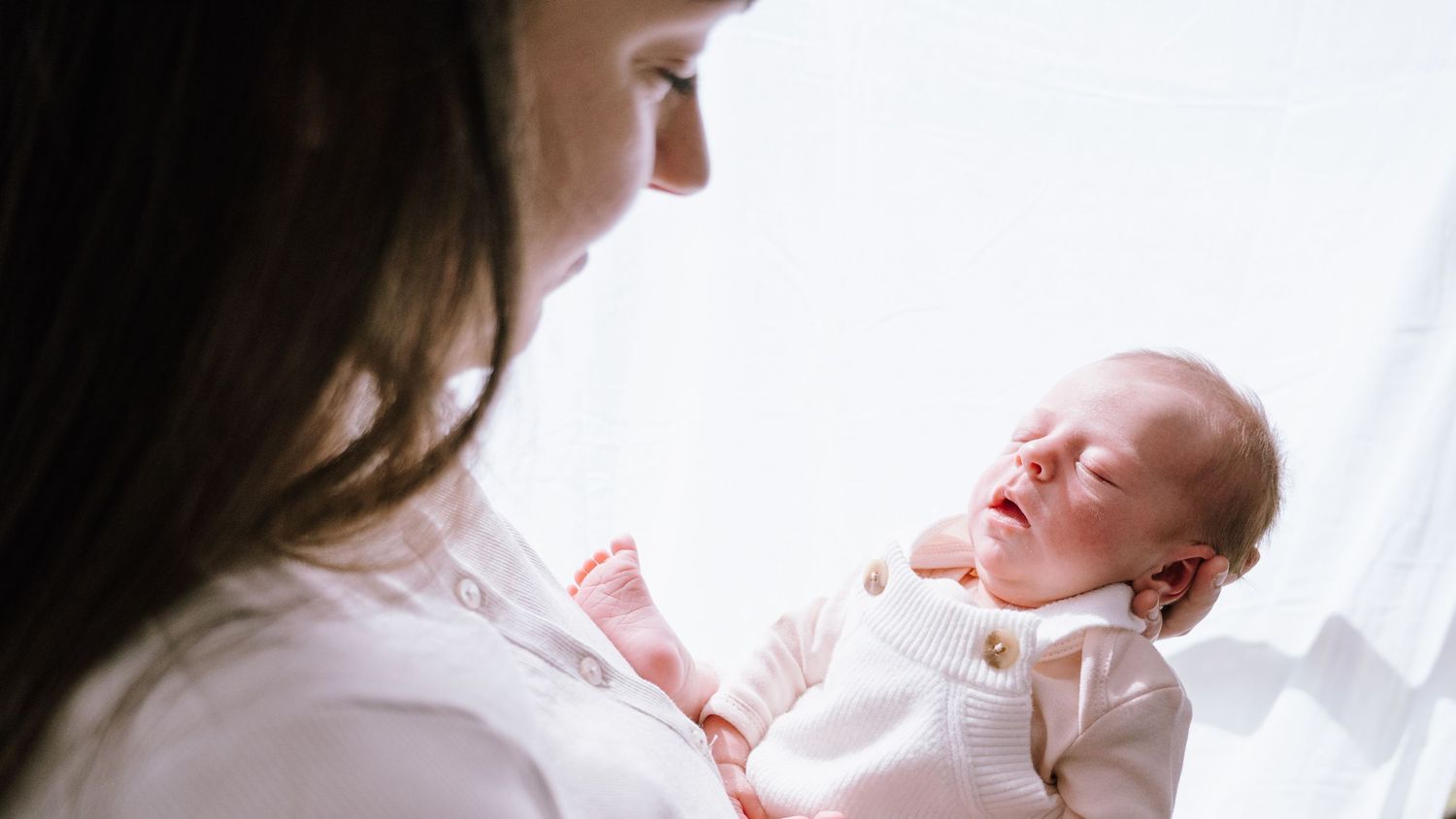 A tender moment between parent and newborn baby in soft natural window light.