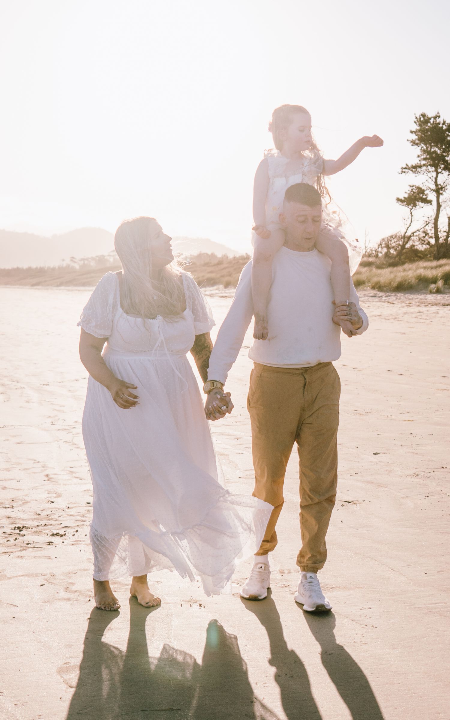 Couple walking hand in hand on sandy beach at sunset casting long shadows in romantic seaside moment.