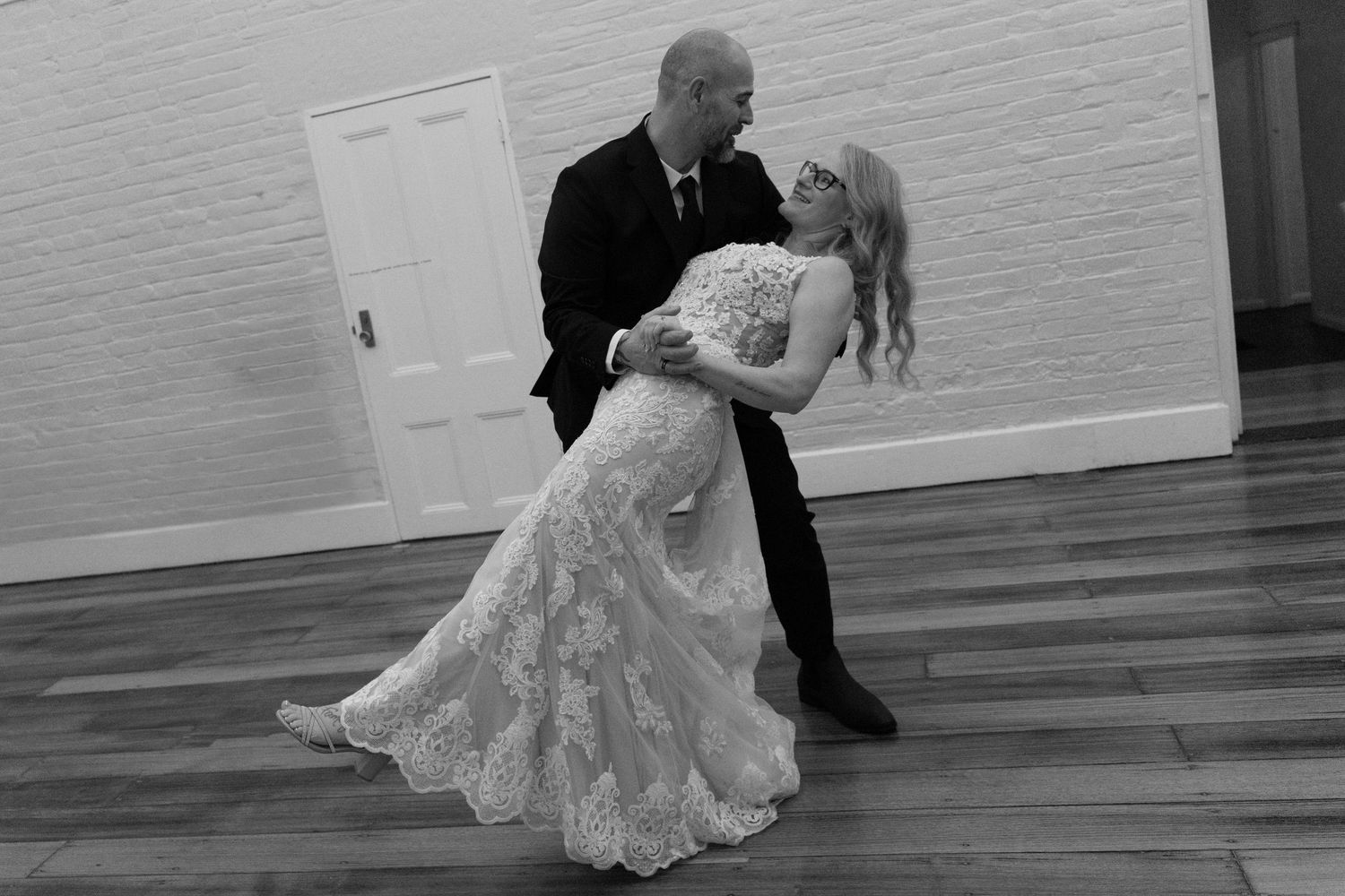 Black and white photo of a bride and groom sharing a romantic first dance dip at their wedding reception.