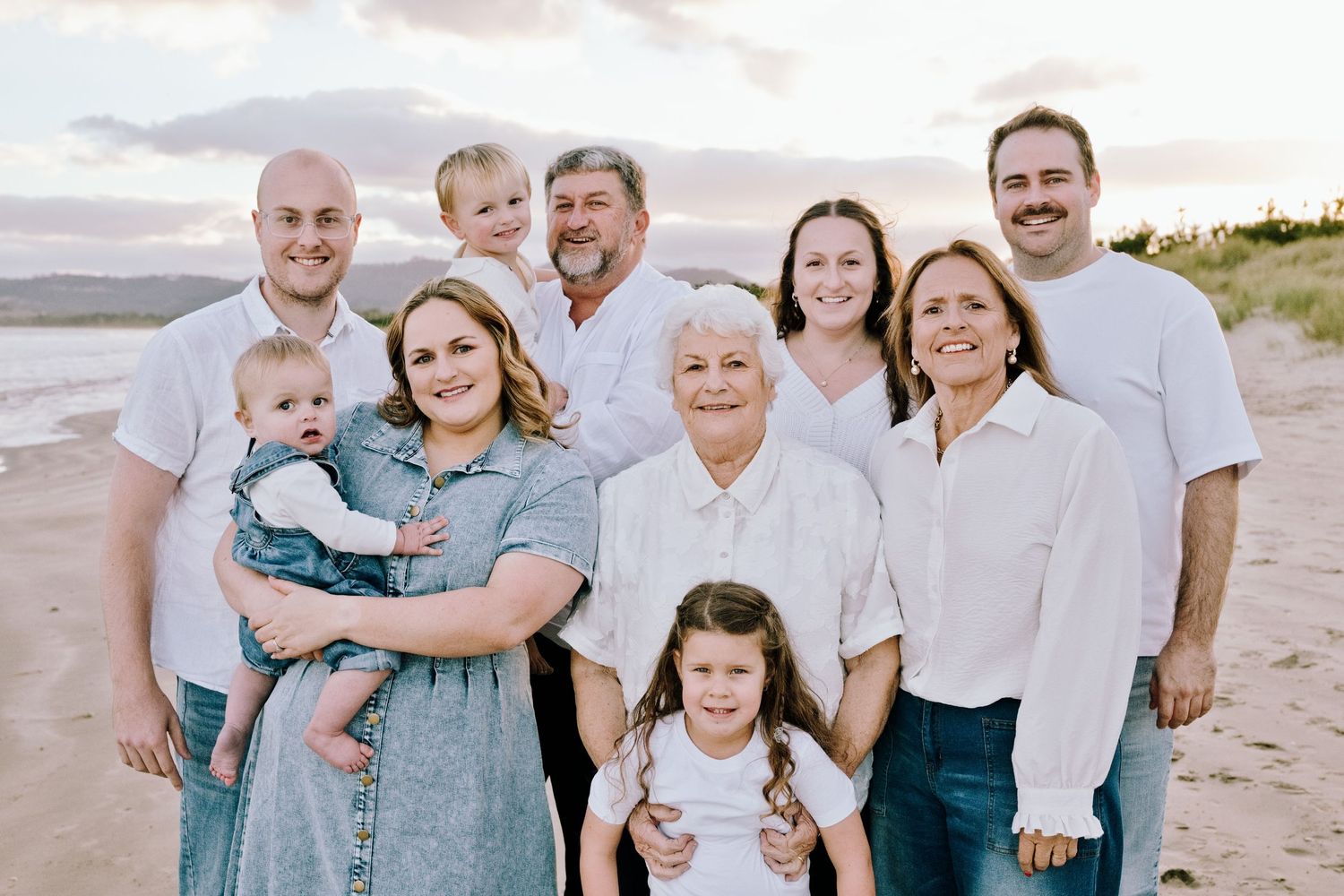Multigenerational family group portrait on a beach at sunset with children and grandparents.