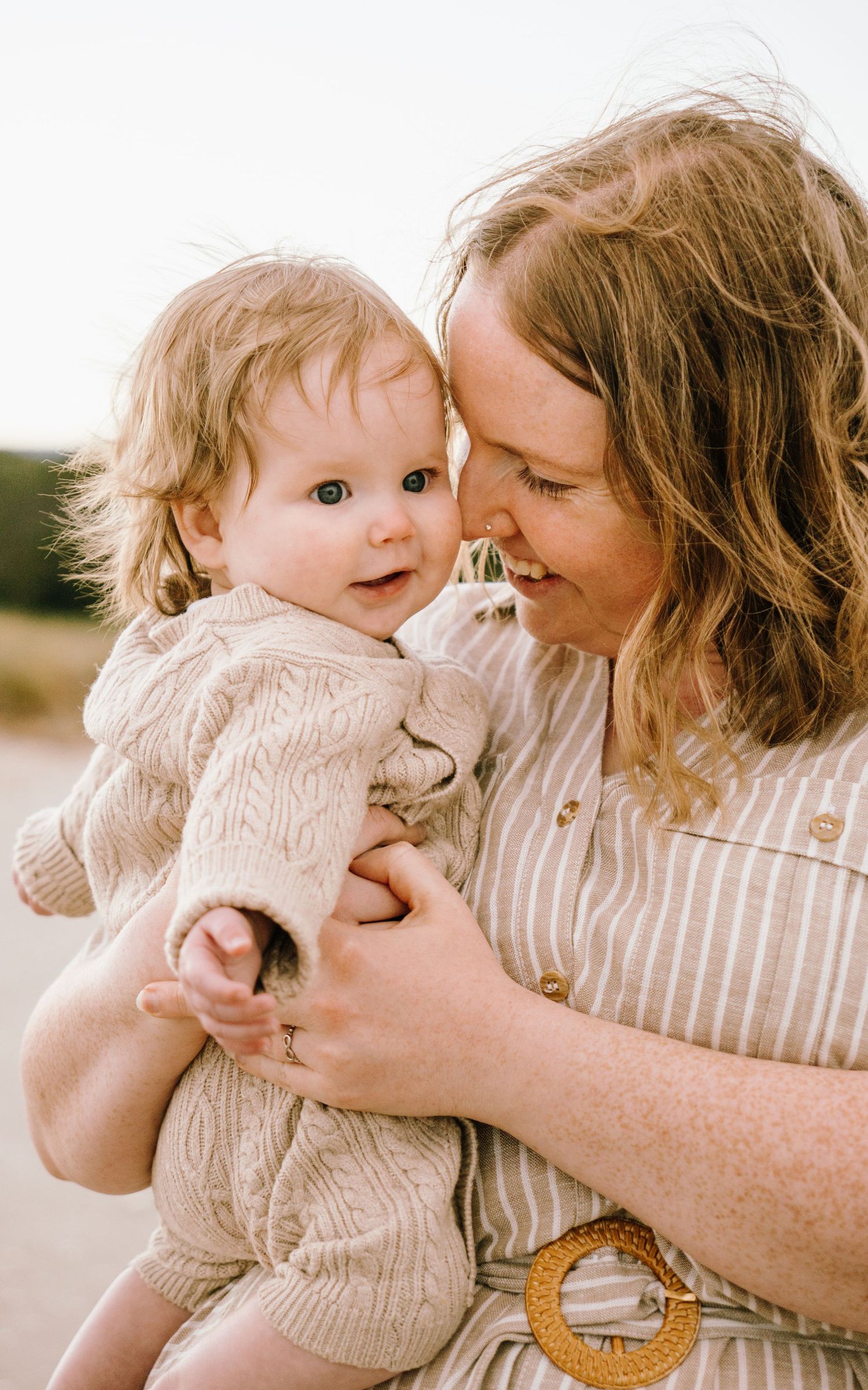 A tender moment between parent and child outdoors in warm sunlight wearing light colored clothing.