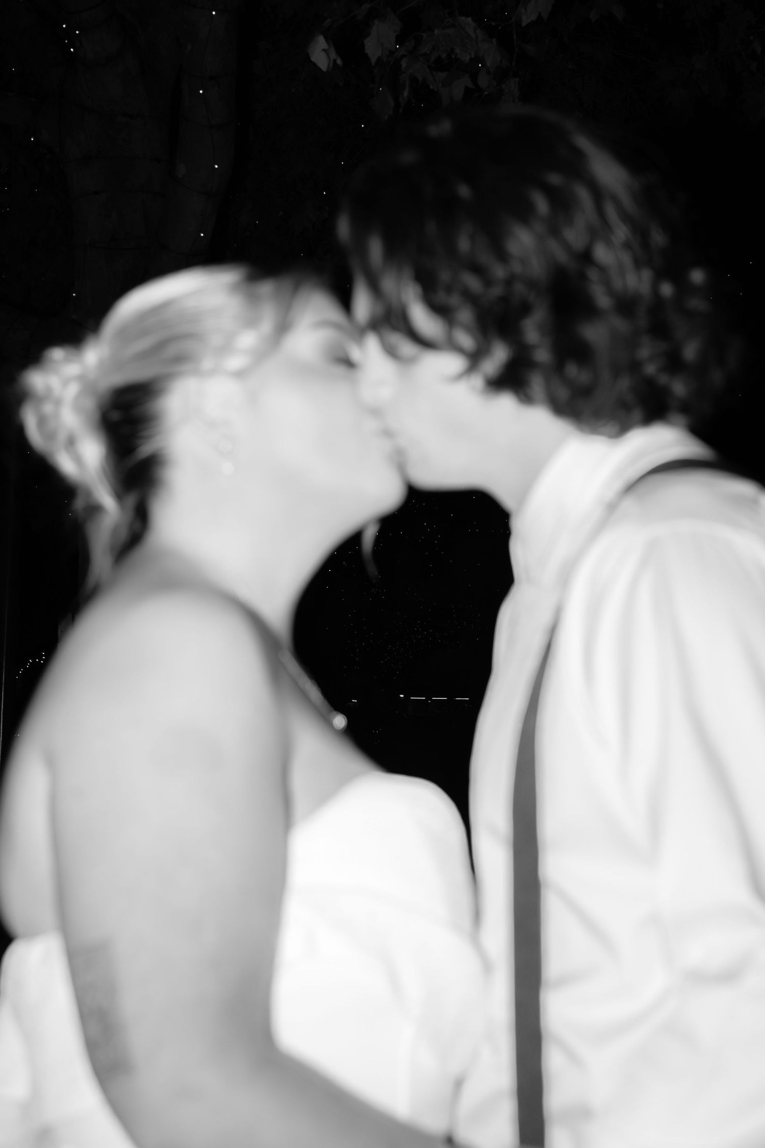 Black and white photo of a bride and groom sharing a romantic kiss at their wedding reception.