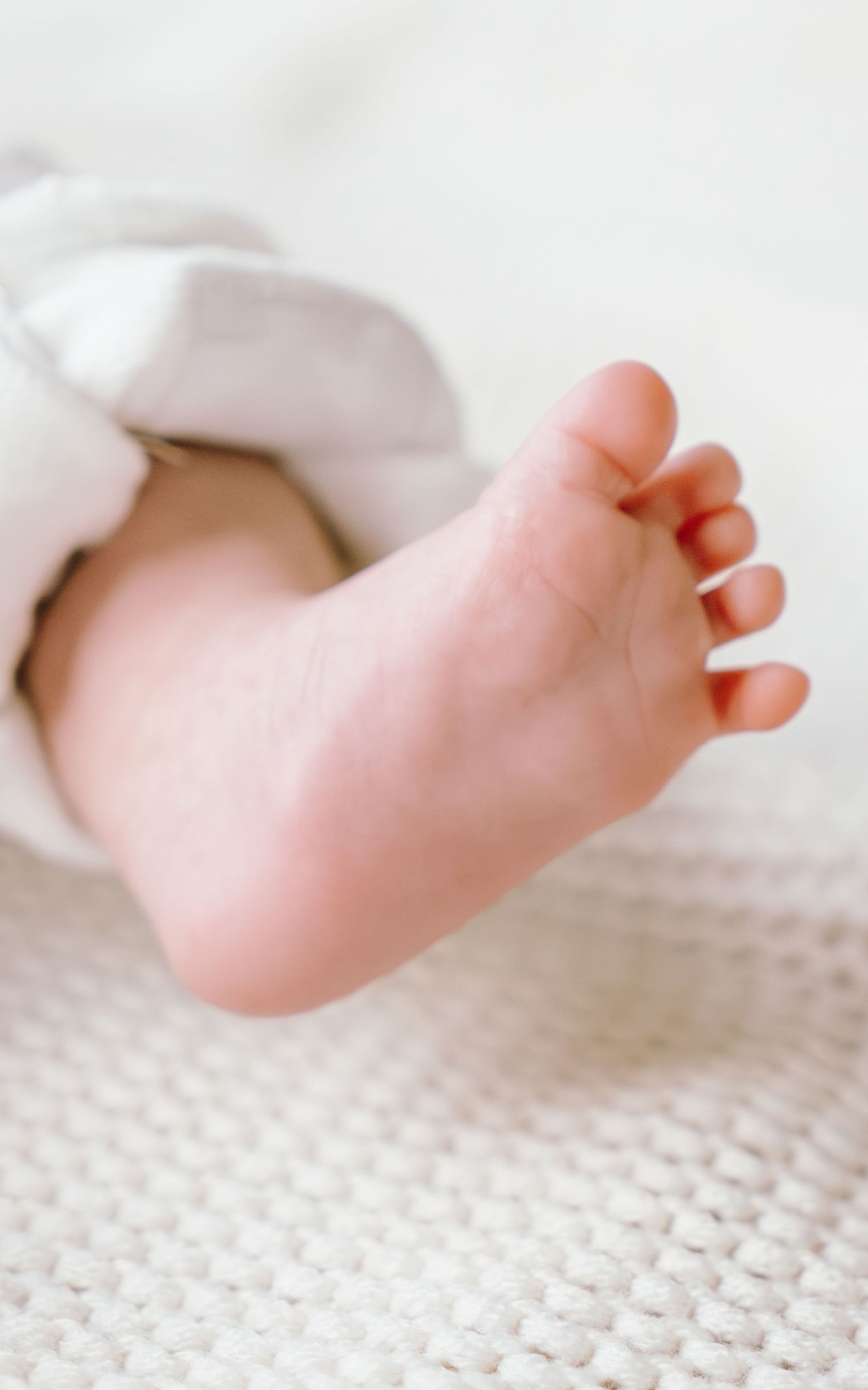 A series of tiny baby feet resting on a white knitted blanket shown from different angles in a soft, gentle light.
