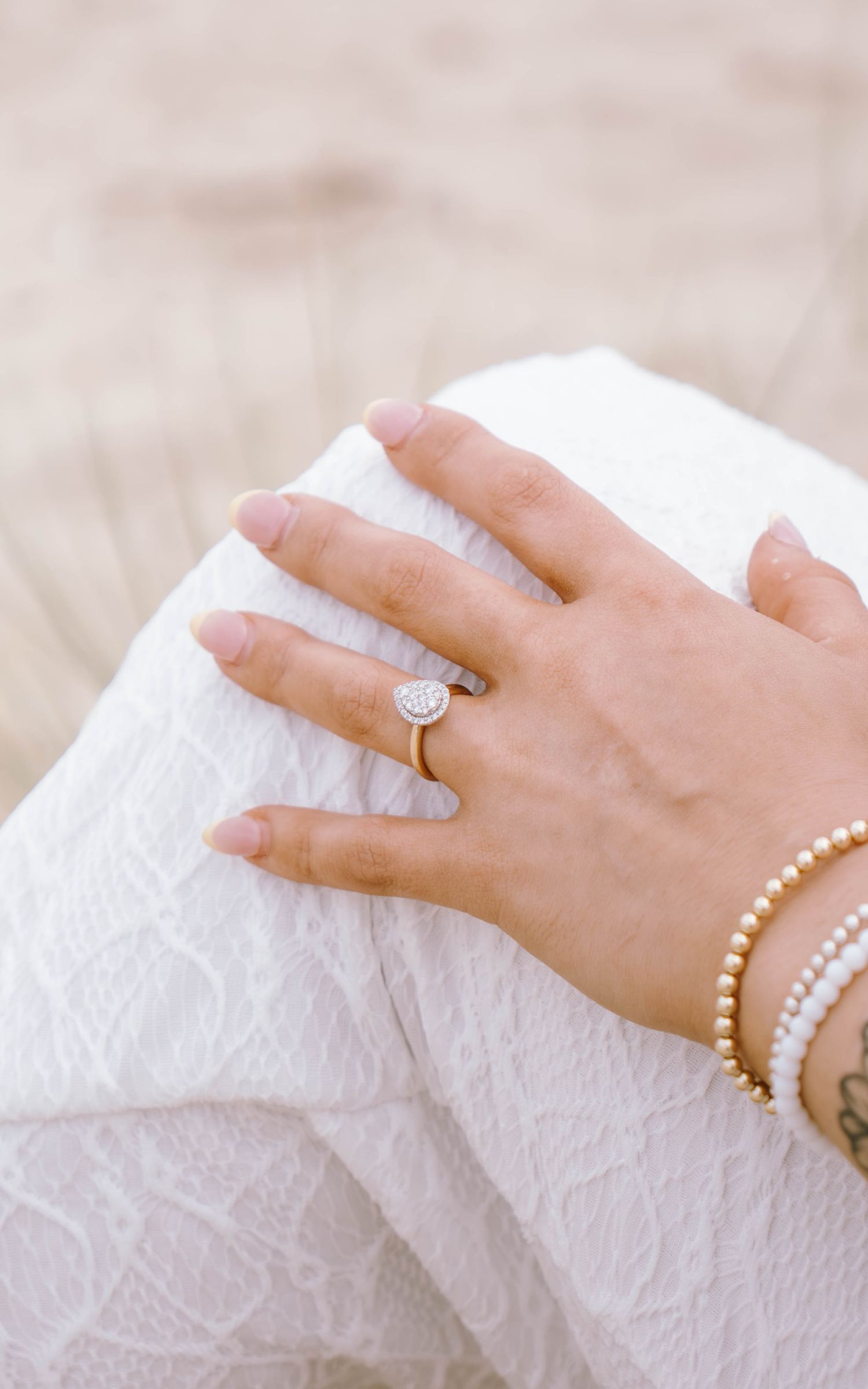 Close-up of hands wearing delicate rings and bracelets against white lace fabric, showcasing elegant bridal jewelry details.